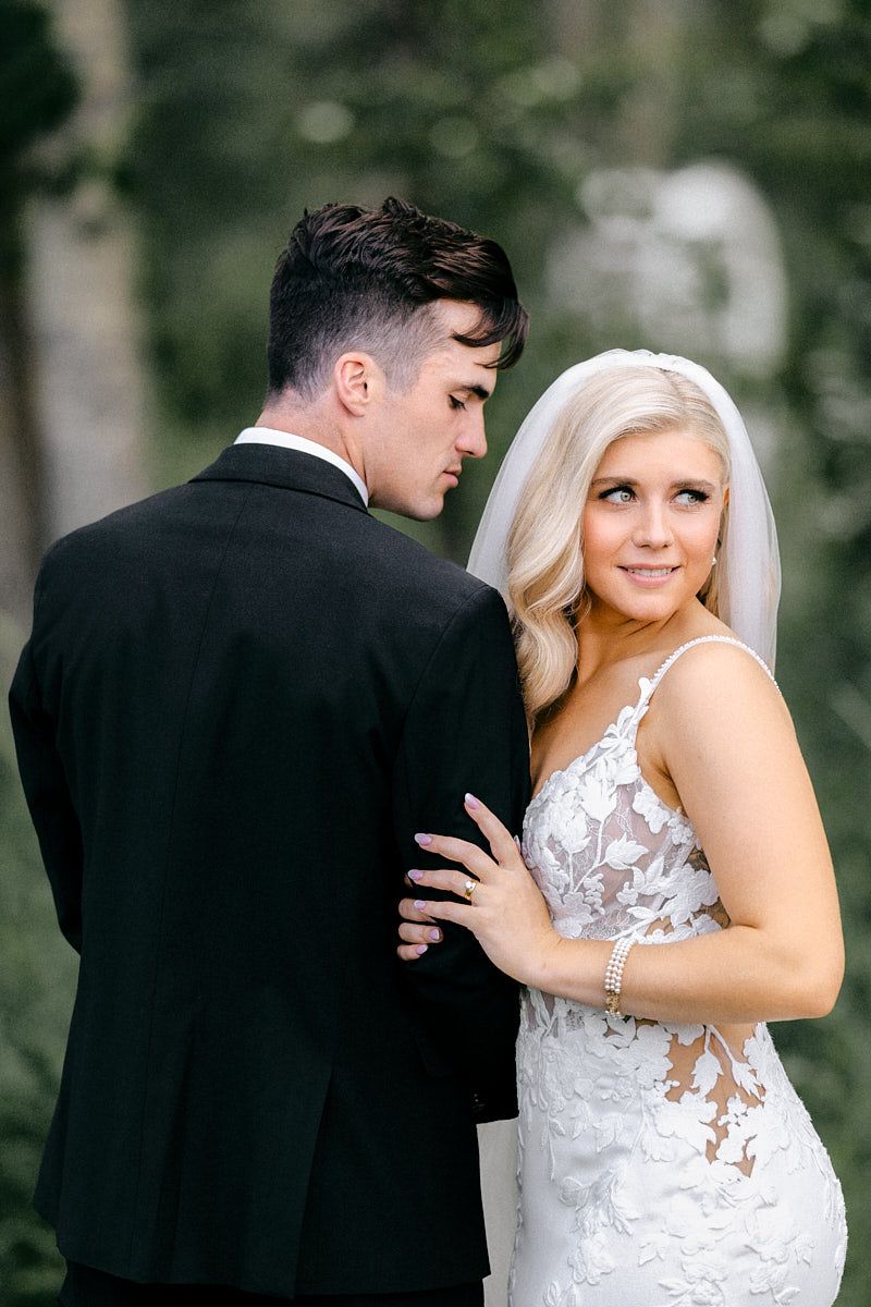 The couple poses against the lush greenery of a Latvian wedding venue, creating a timeless wedding image.