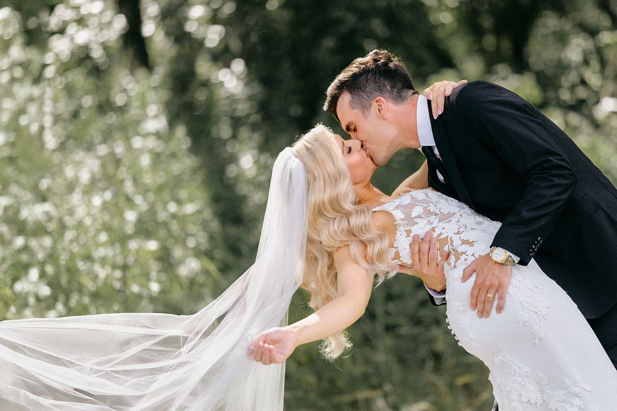 Romantic couple dip kissing in the lush forests in Riga, surrounded by vibrant greenery.