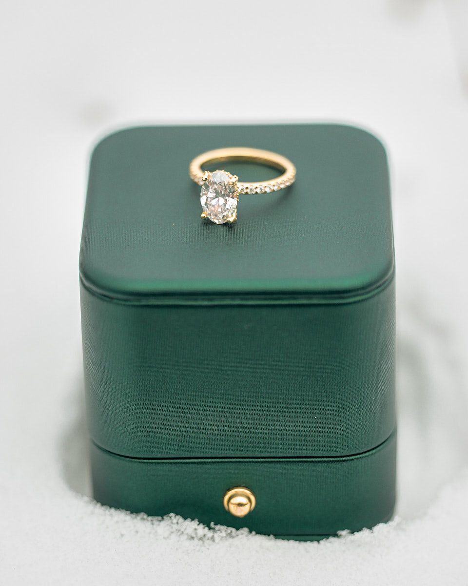 Diamond wedding ring on green ring box in snow, winter engagement detail