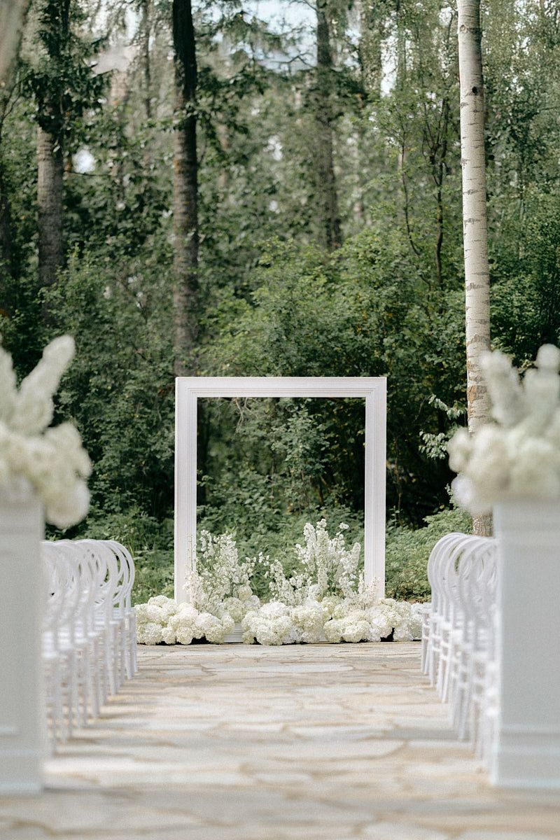 A breathtaking outdoor ceremony setup in Riga, featuring white chairs and lush floral arrangements.