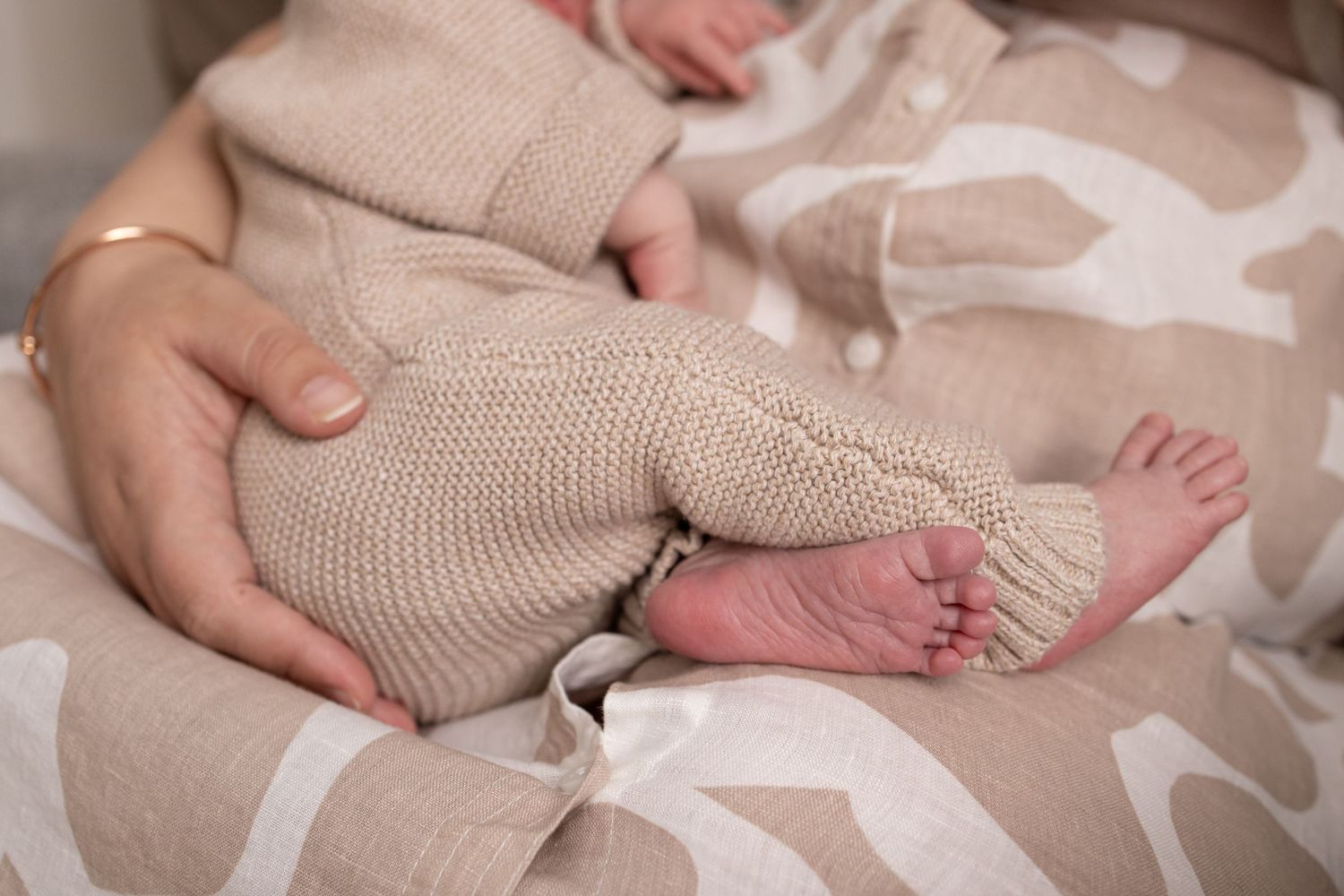 Close-up of tiny newborn feet wrapped in soft beige knit romper in natural light setting.