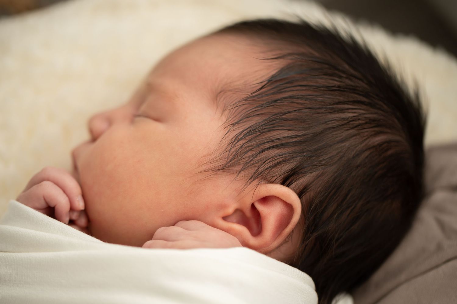 Close-up of sleeping newborn with dark hair on soft bedding.