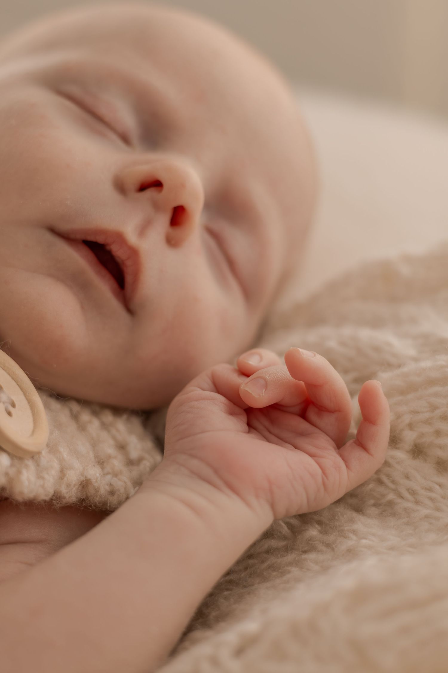 Sleeping baby in knit clothing with tiny hand curled on beige blanket.