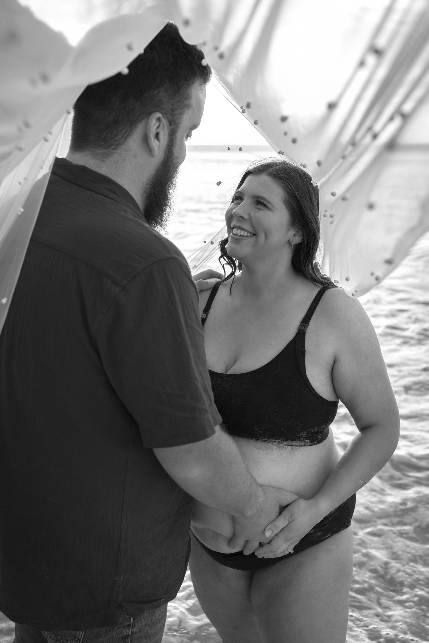 A black and white beach portrait of a couple sharing a tender moment together underneath bridal veil.