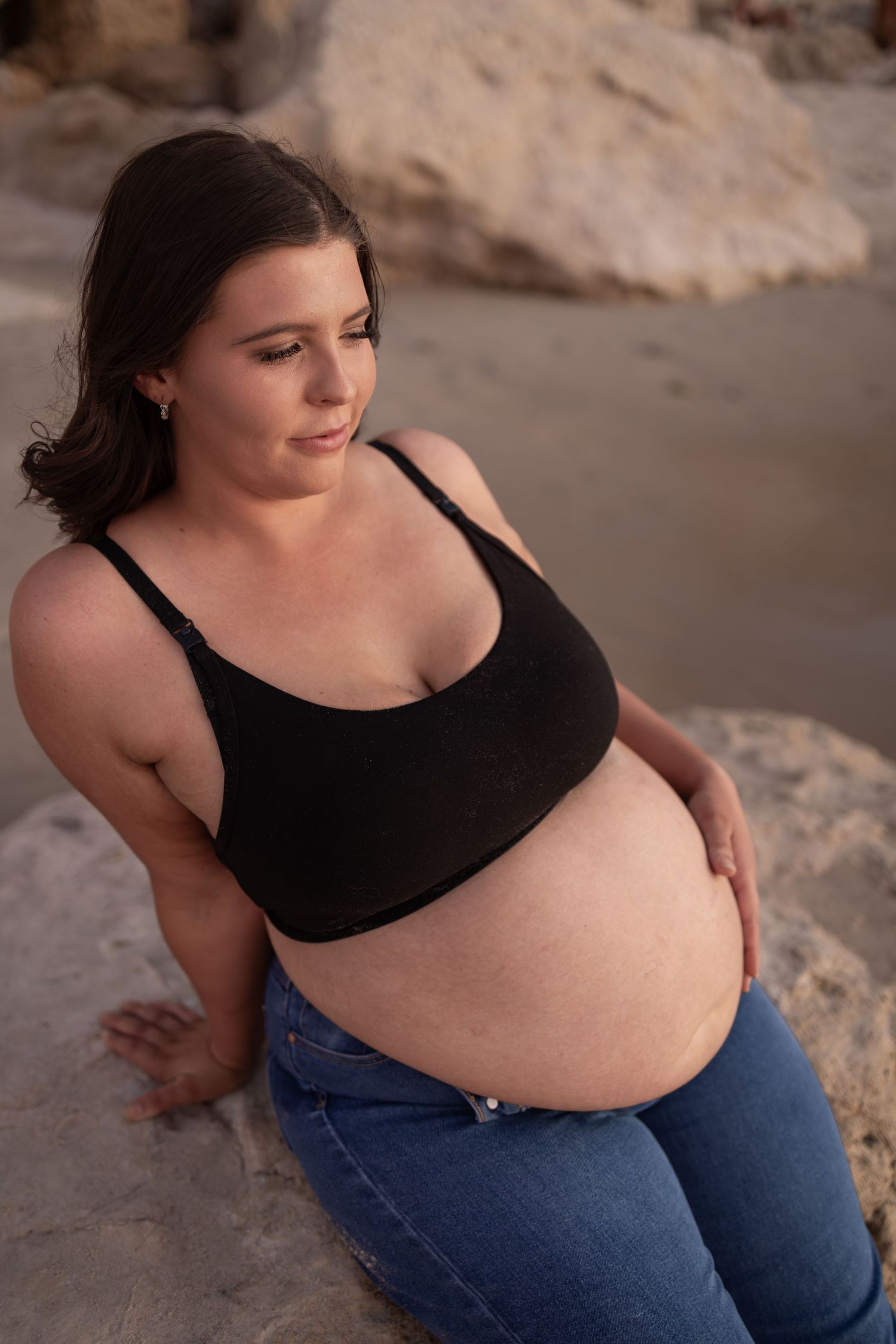 Maternity portrait on rocky beach with warm sunset lighting and coastal cliffs.