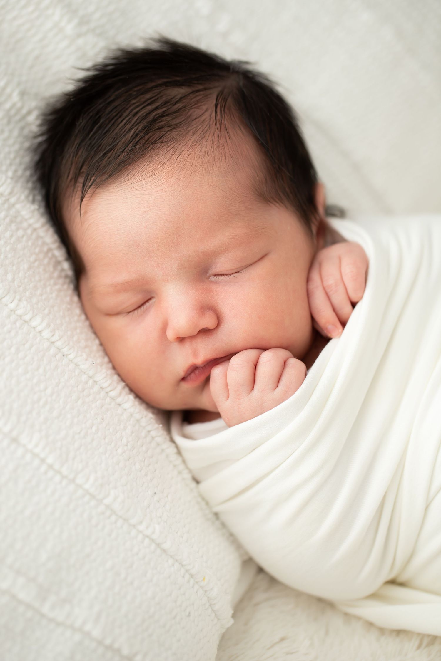 Close-up of peaceful sleeping baby swaddled in white fabric.