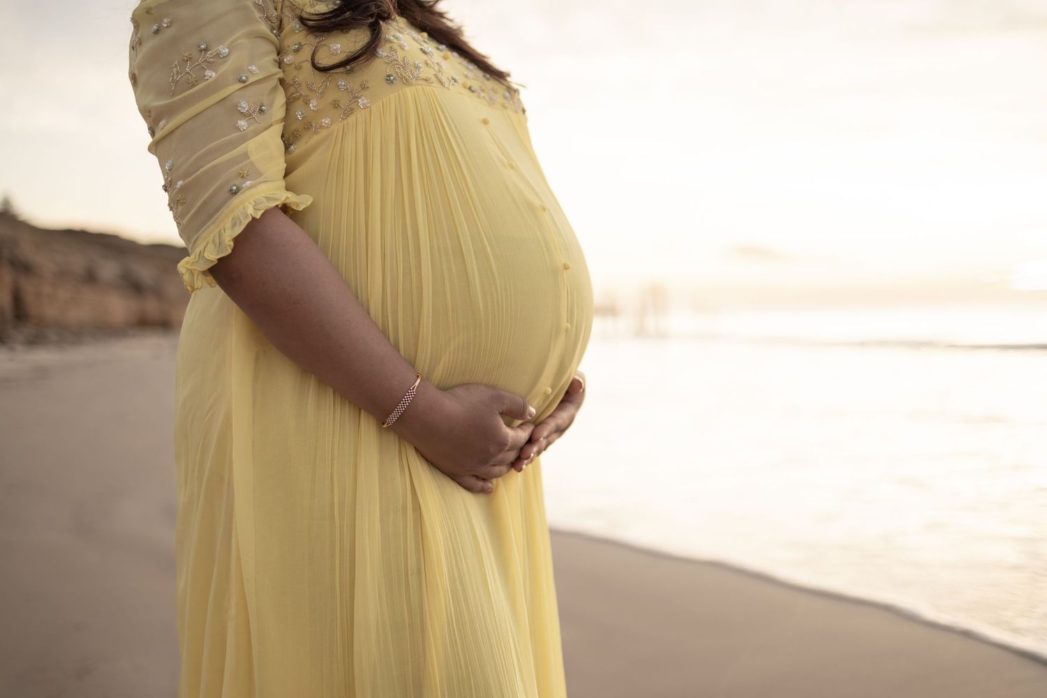 Expectant mother in flowing yellow dress poses at sunset.
