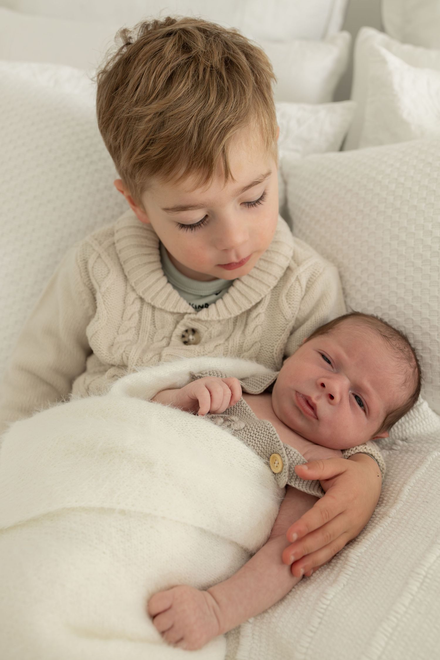 Two siblings sharing tender moment together on white bedding.
