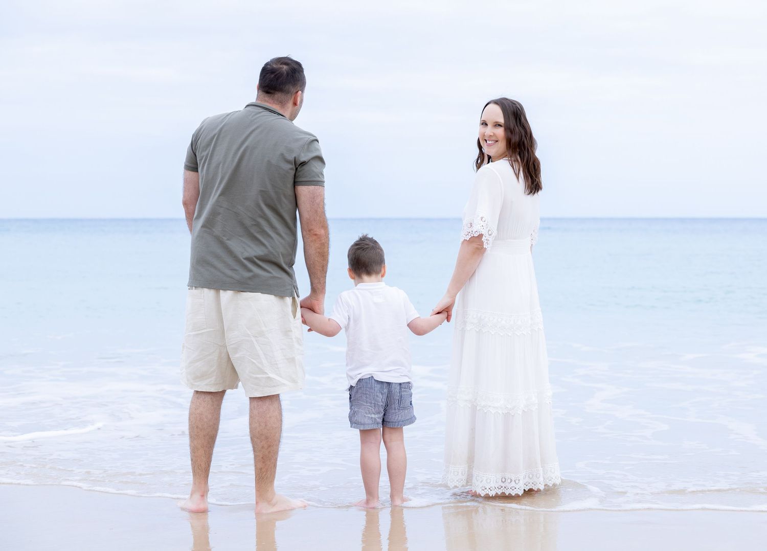 Family in white and neutral clothing walking together on pristine beach.