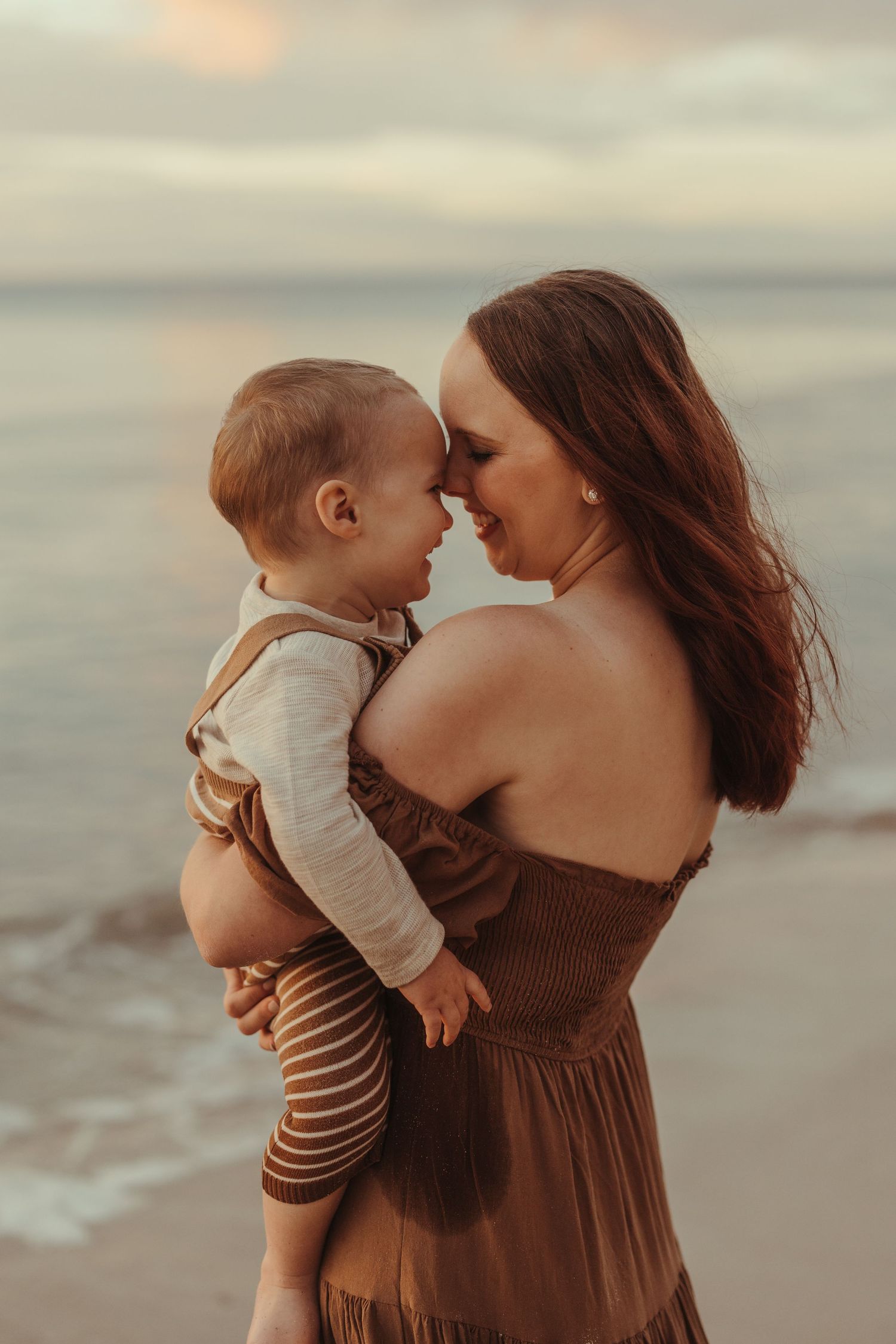 Gentle embrace between mother and son captured at sunset on sandy beach.