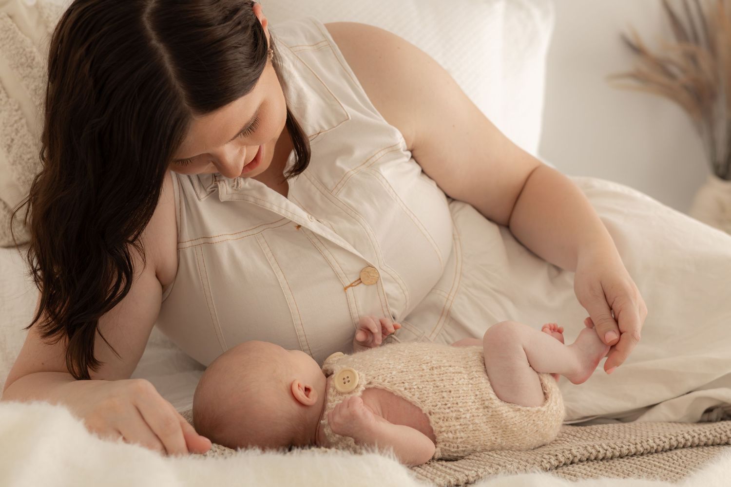A tender moment between mother and infant lying on soft beige bedding.
