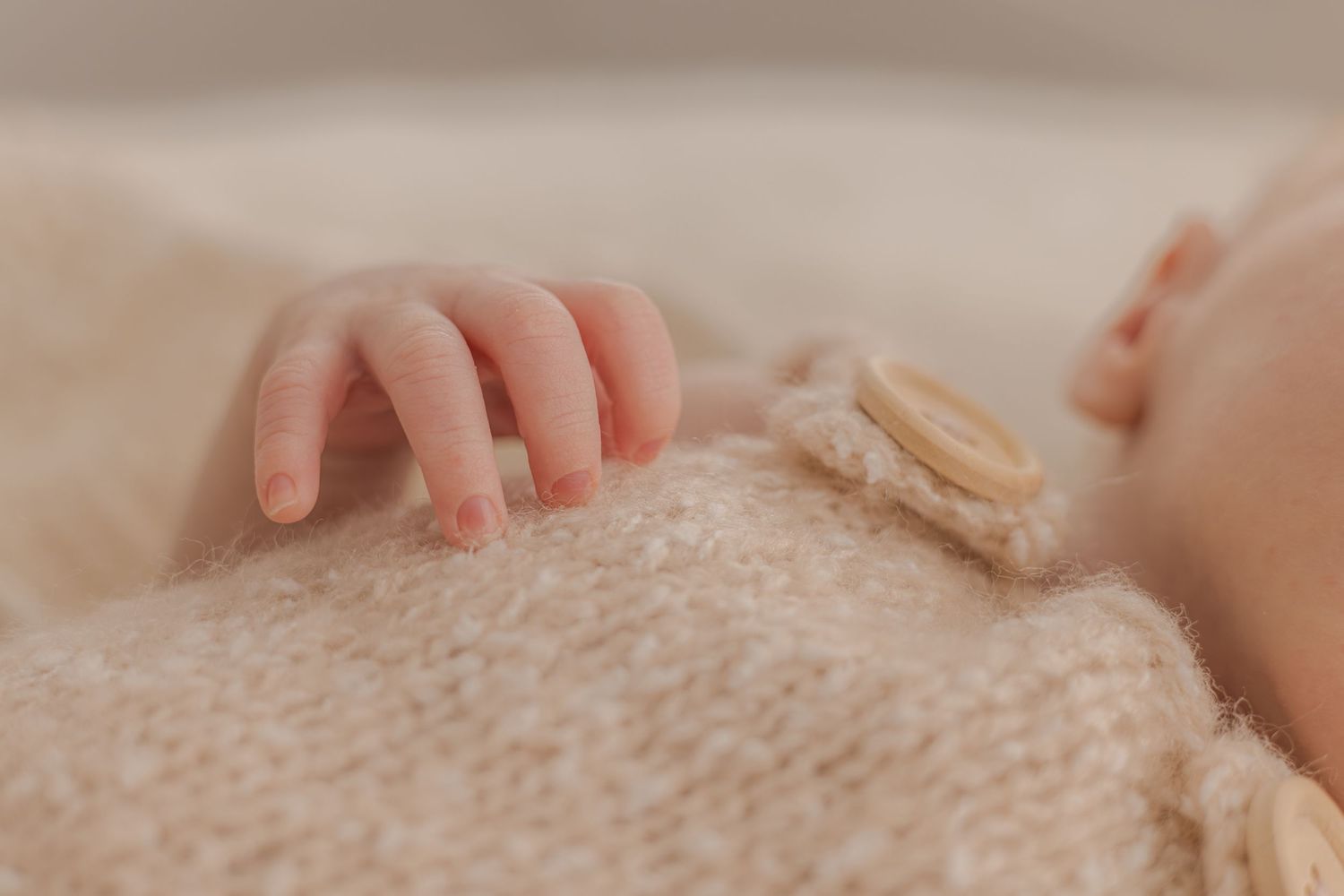 Close up detail of baby's tiny hands on textured knit fabric.