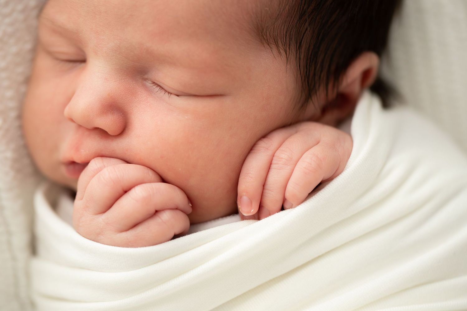 Artistic series of newborn portraits showing baby wrapped in white.