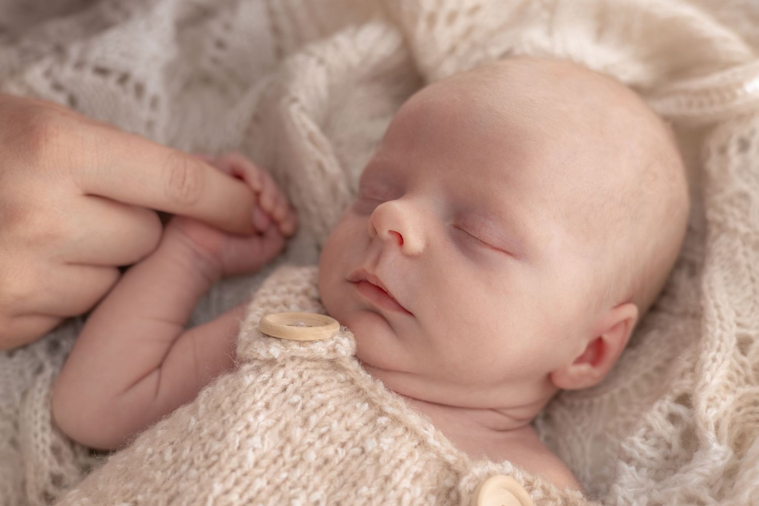 Peaceful sleeping newborn baby wrapped in soft knit blanket during professional photoshoot.