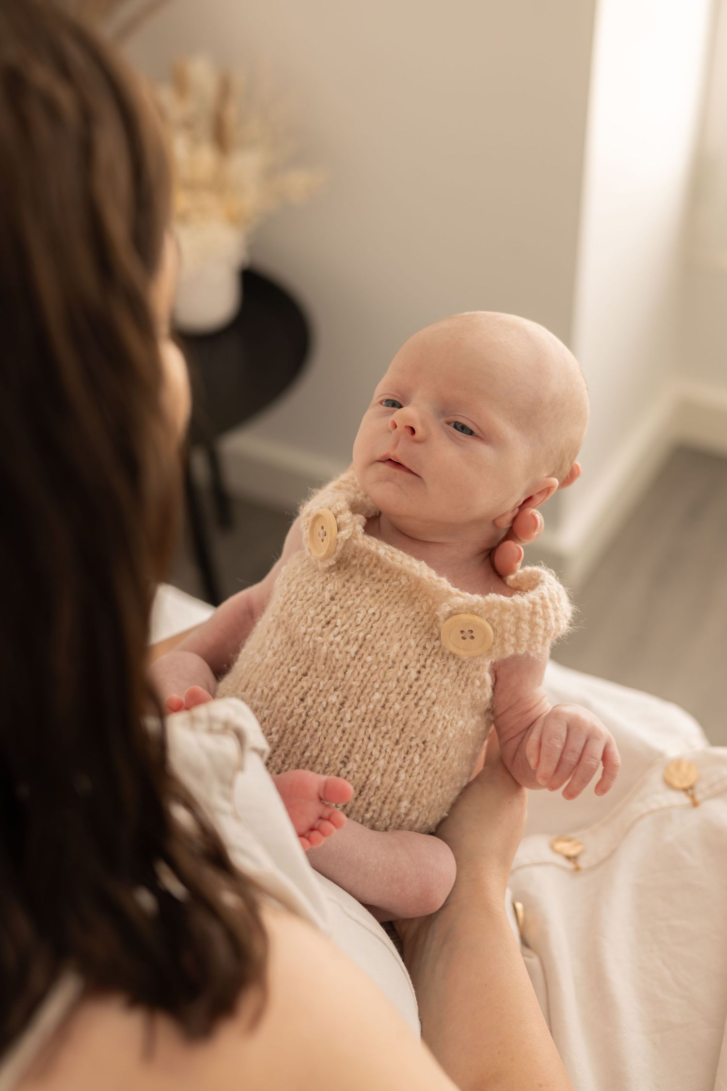 Infant wearing beige knitted romper outfit being held by mother during photo session.