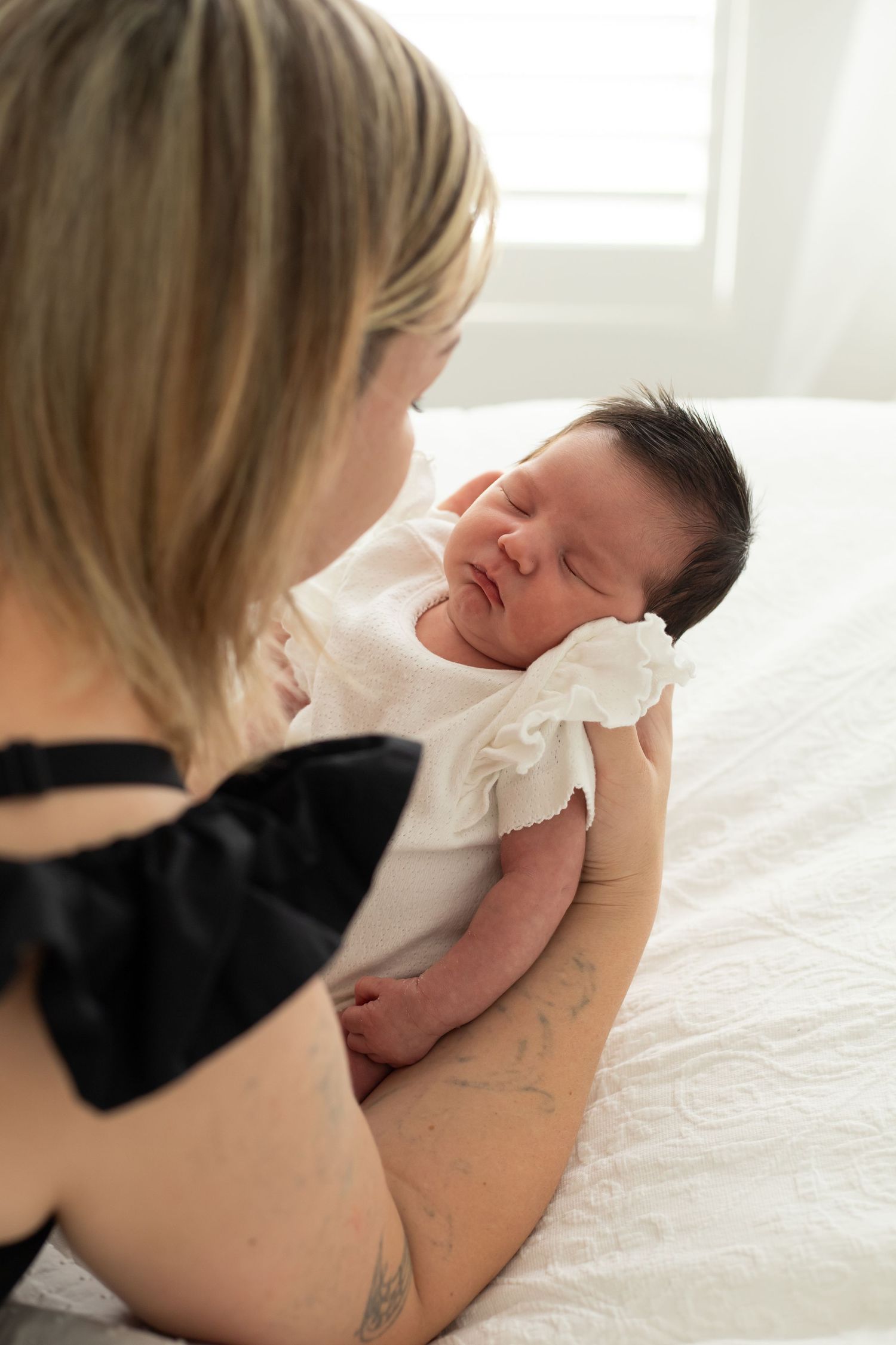 Tender moment between mother and newborn baby on white bed.