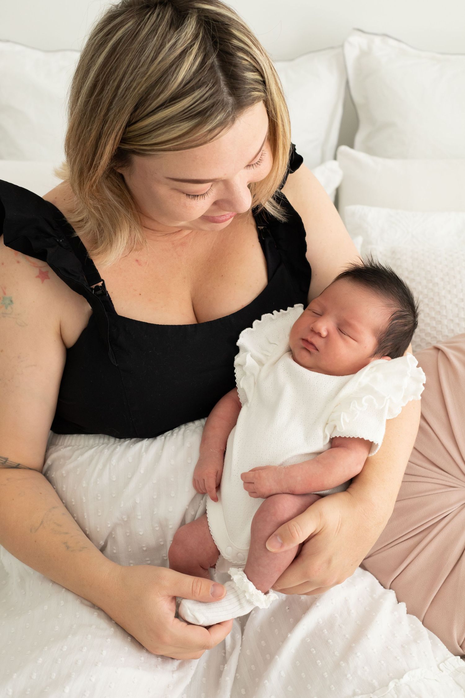 Mother in black top holding newborn baby on white bedding.