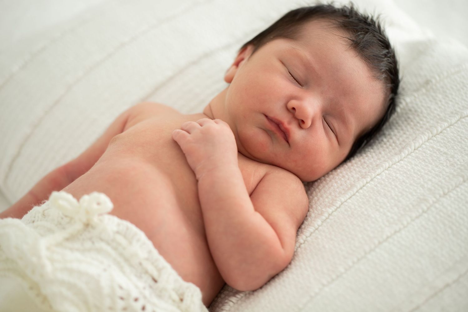Newborn baby wearing knitted bloomers sleeping on white textured surface in natural light.
