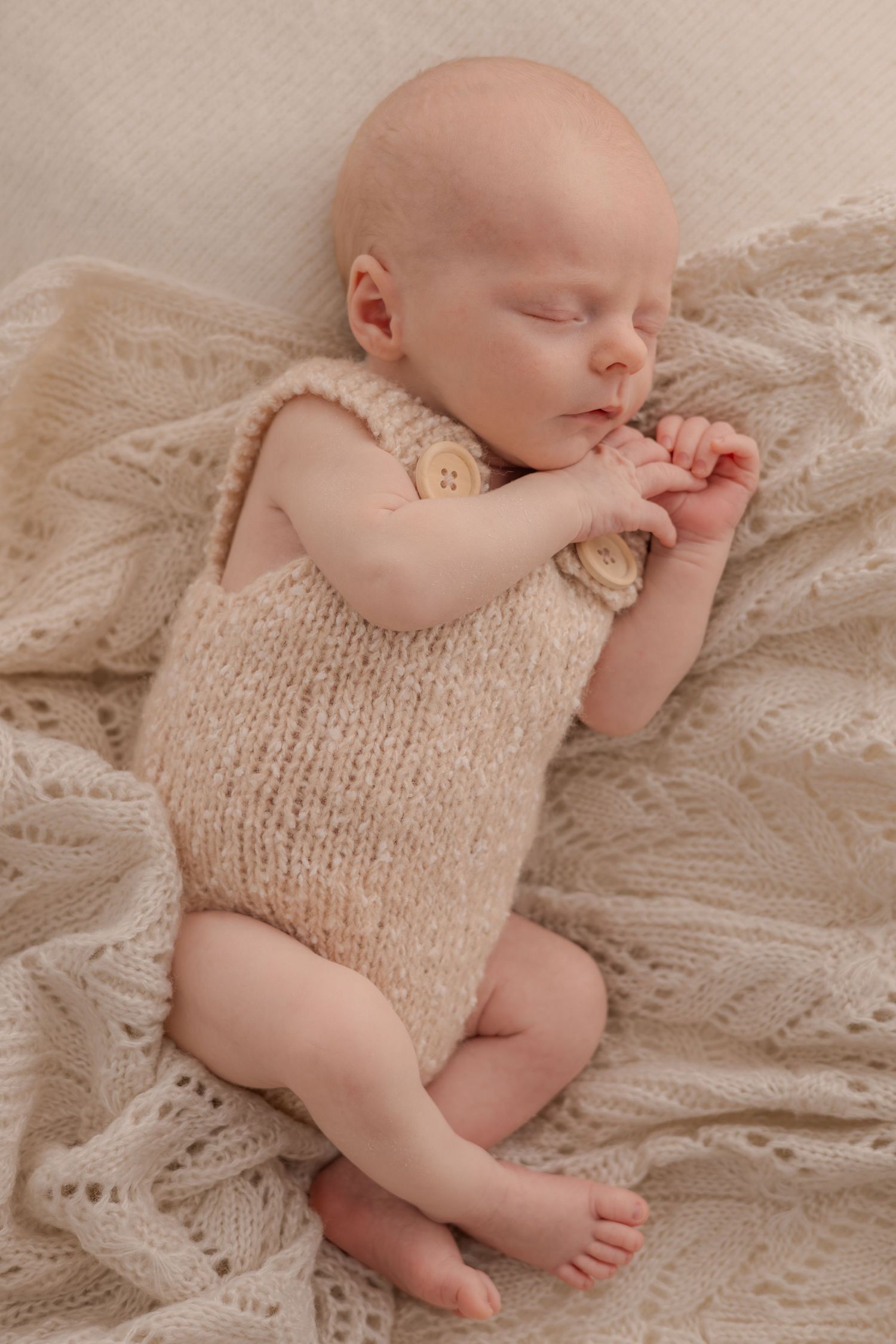 Peaceful sleeping baby in beige knit romper on delicate lace blanket.