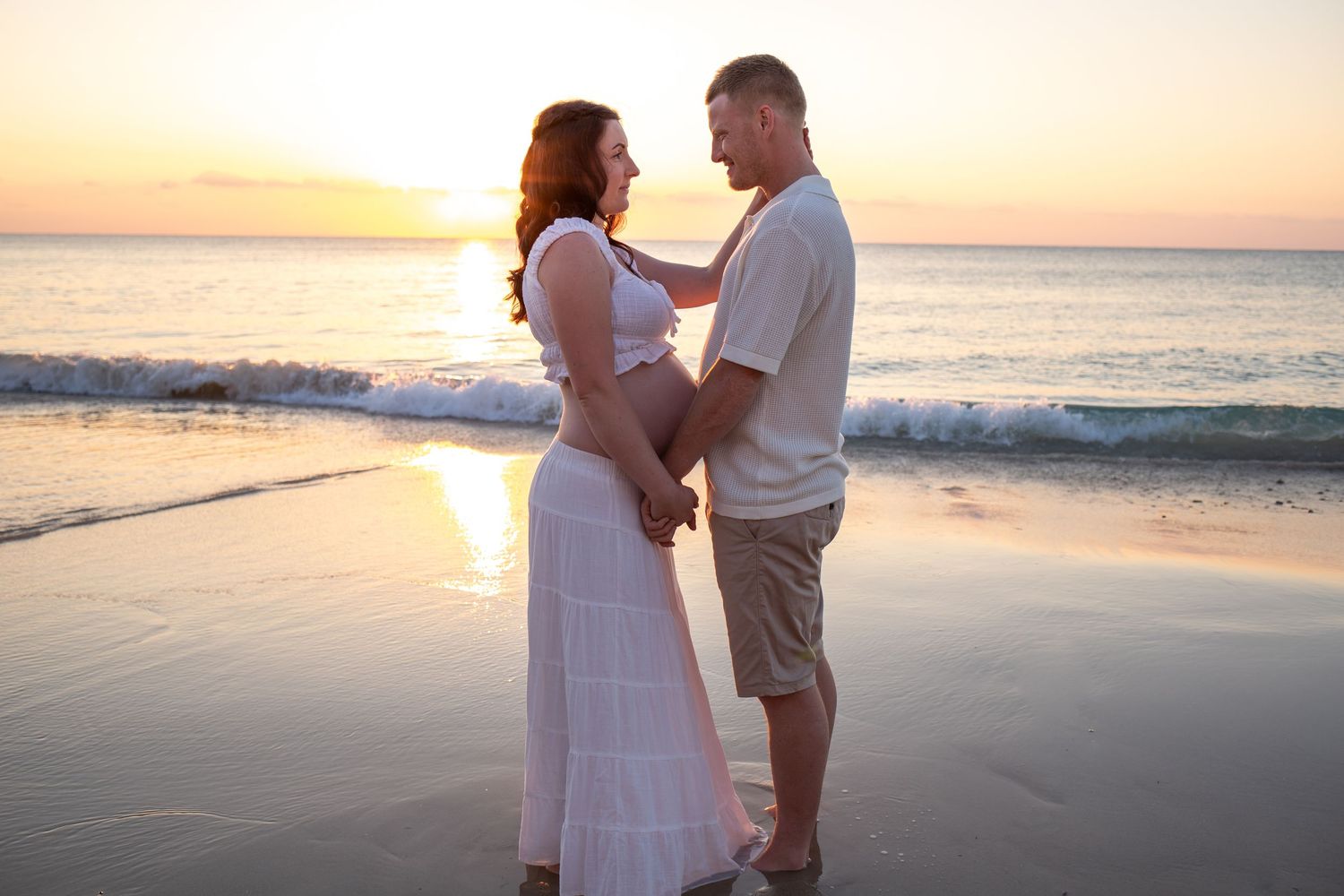 A romantic maternity photo of a couple embracing on the beach during golden hour.