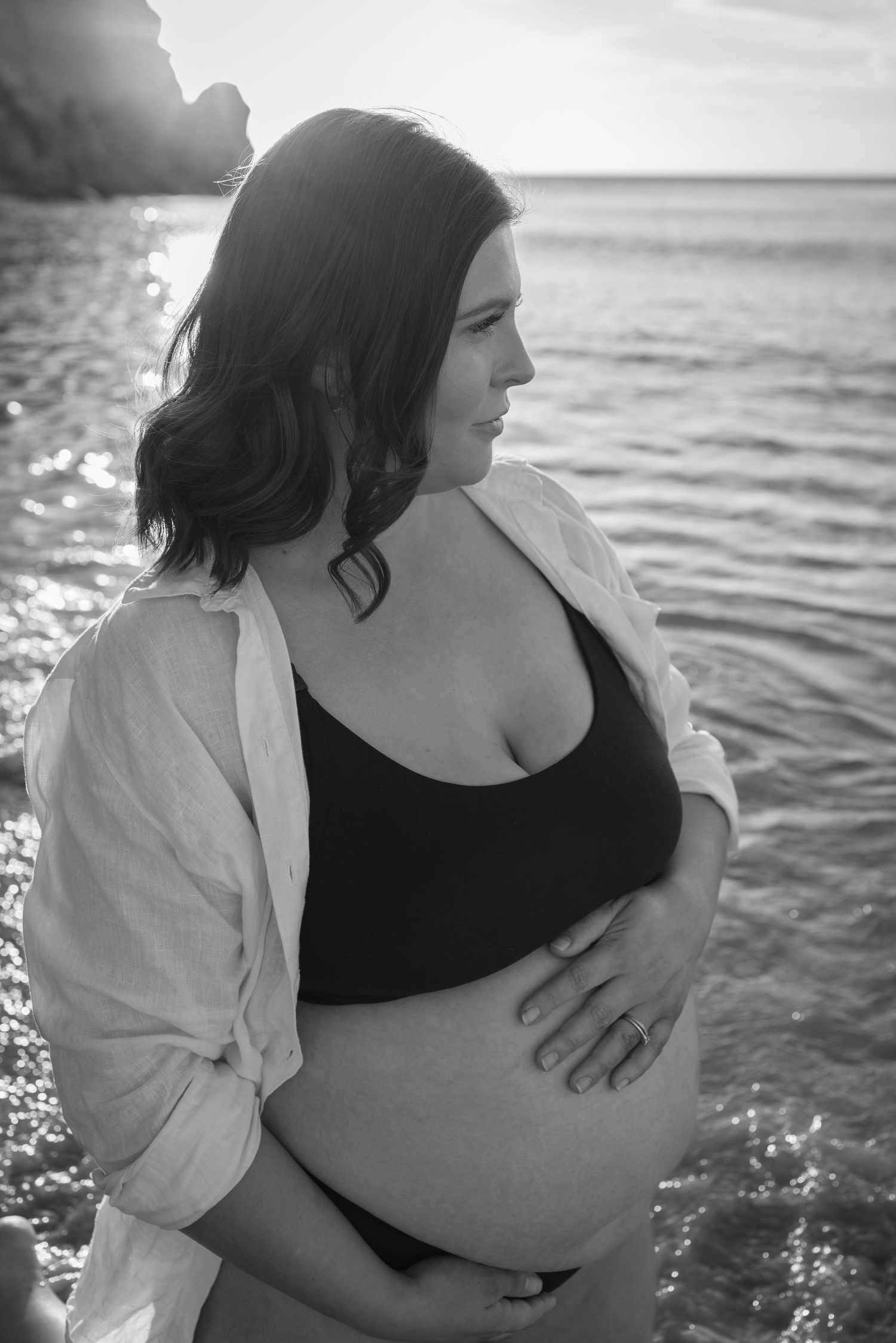 Black and white maternity photos on beach with waves and rocks in background.