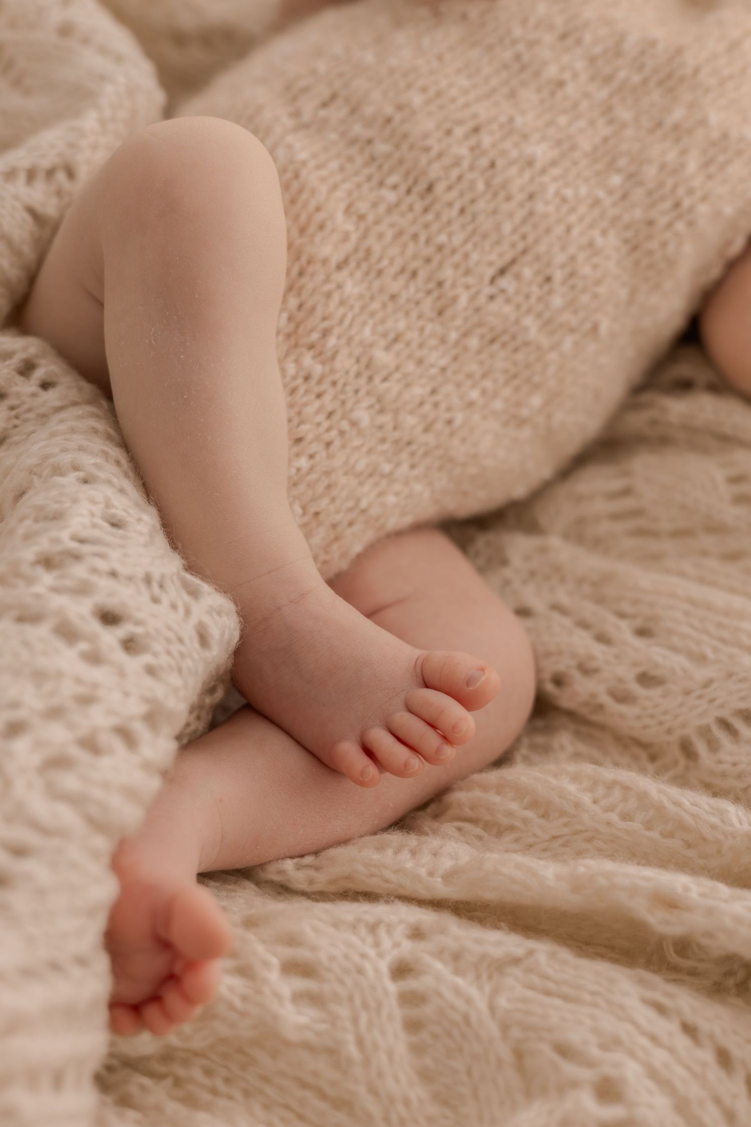 Close up of baby's feet resting on cream colored knitted blanket with lace detail.