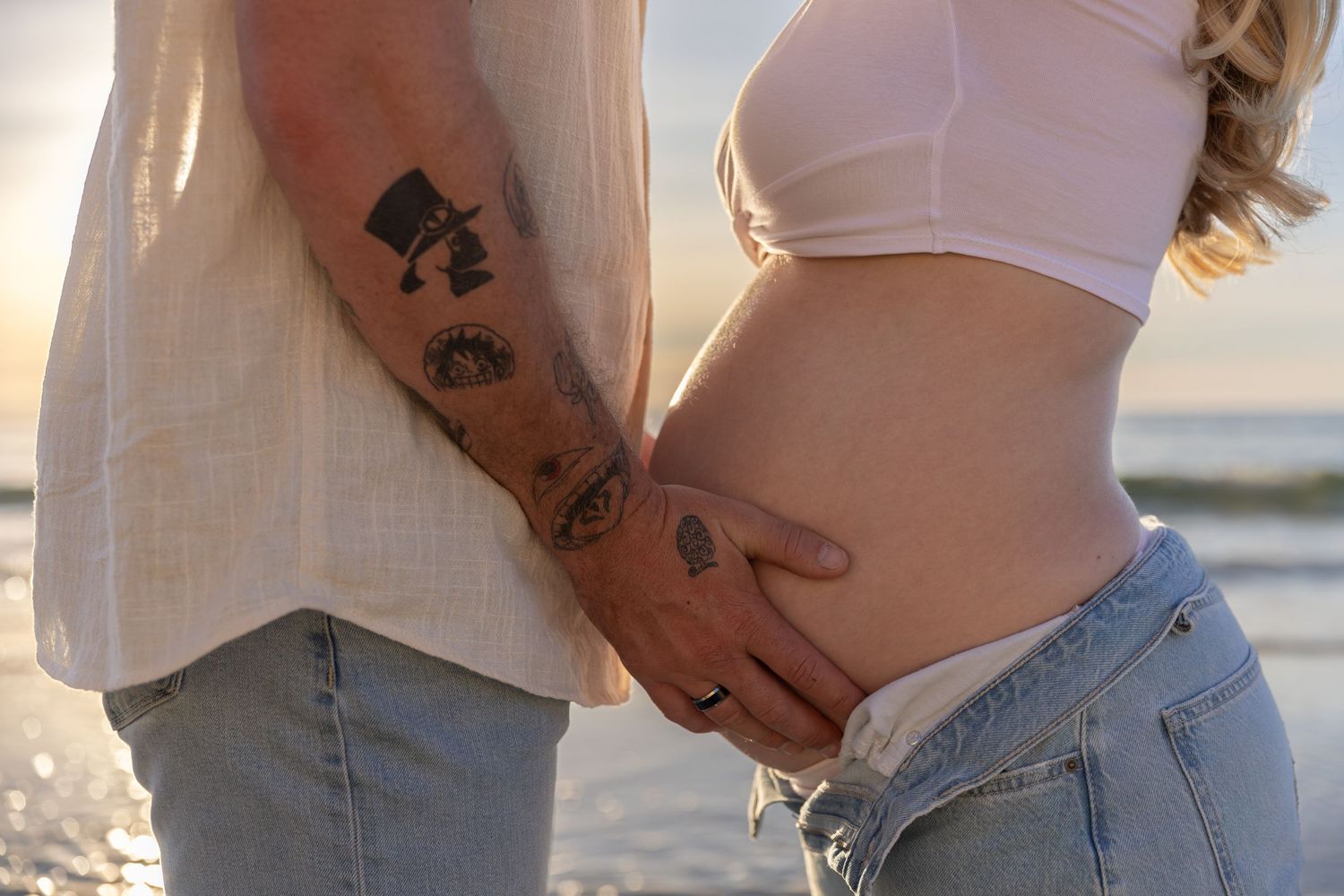 Casual beach maternity photos showing pregnant belly in white crop top and jeans.