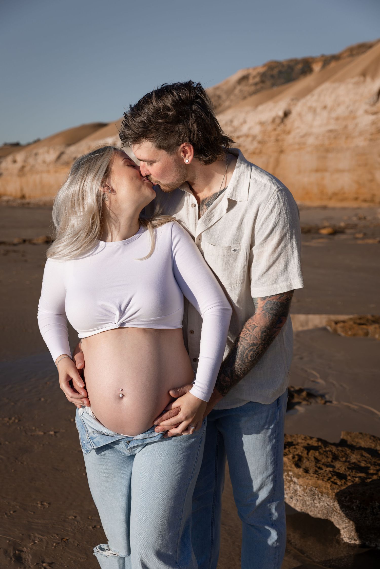 Candid maternity beach photos of couple with coastal cliffs in background.