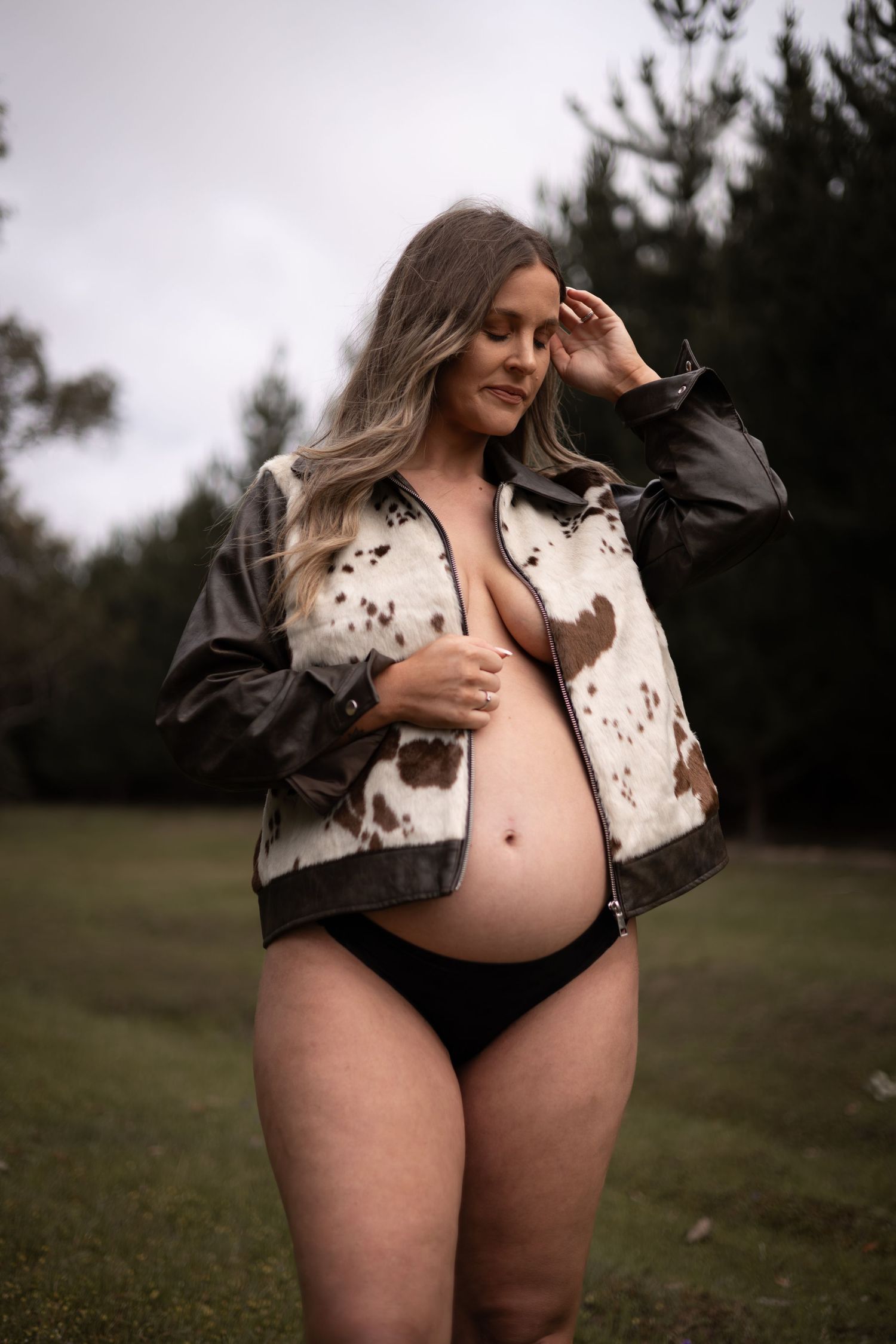 Intimate maternity portrait in field with mother wearing cow print jacket open, showing baby bump.