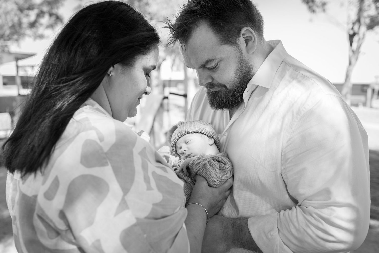 Black and white photo of parents tenderly cradling their newborn baby outdoors.