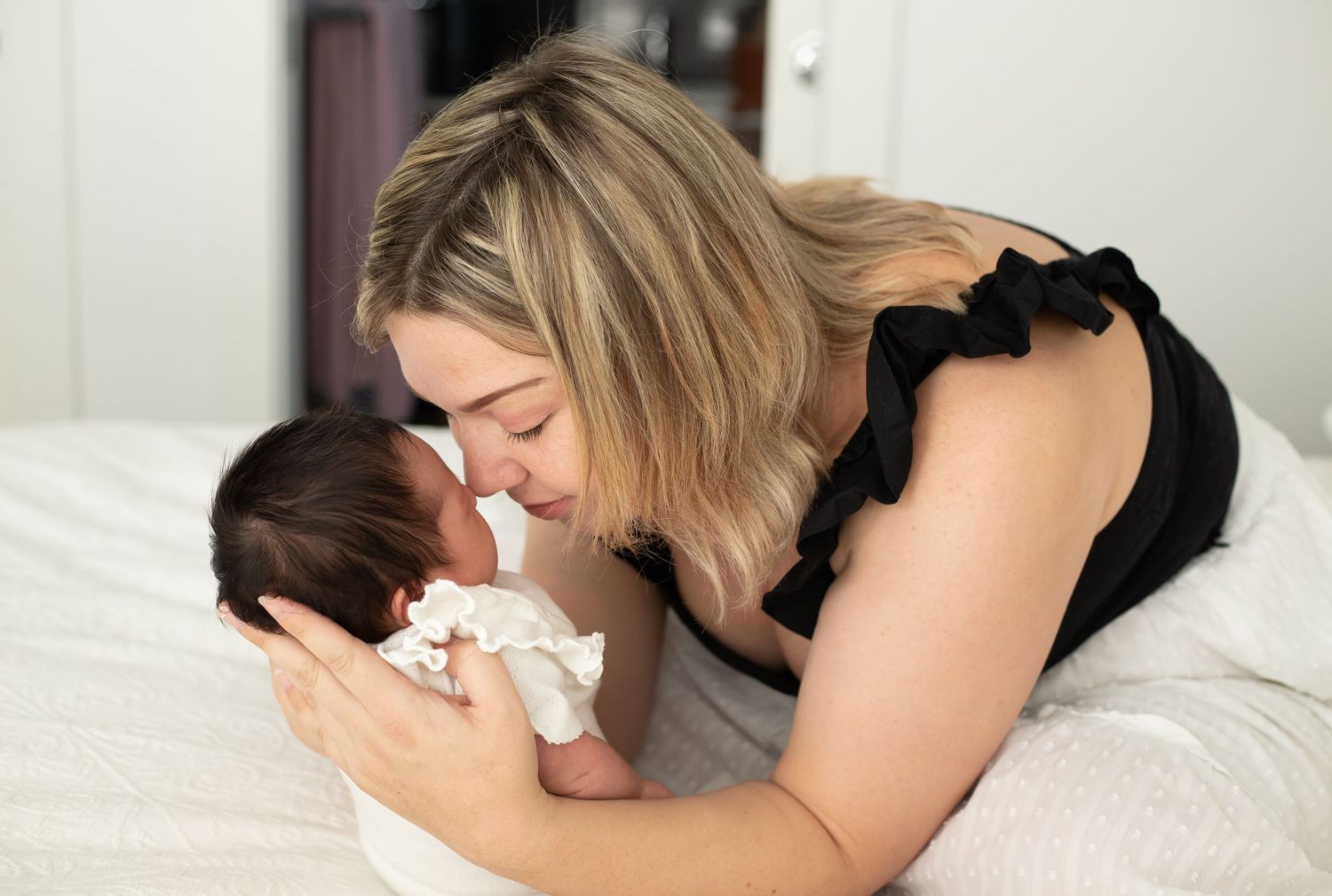 Intimate bonding moment between mother and newborn on white bedding.