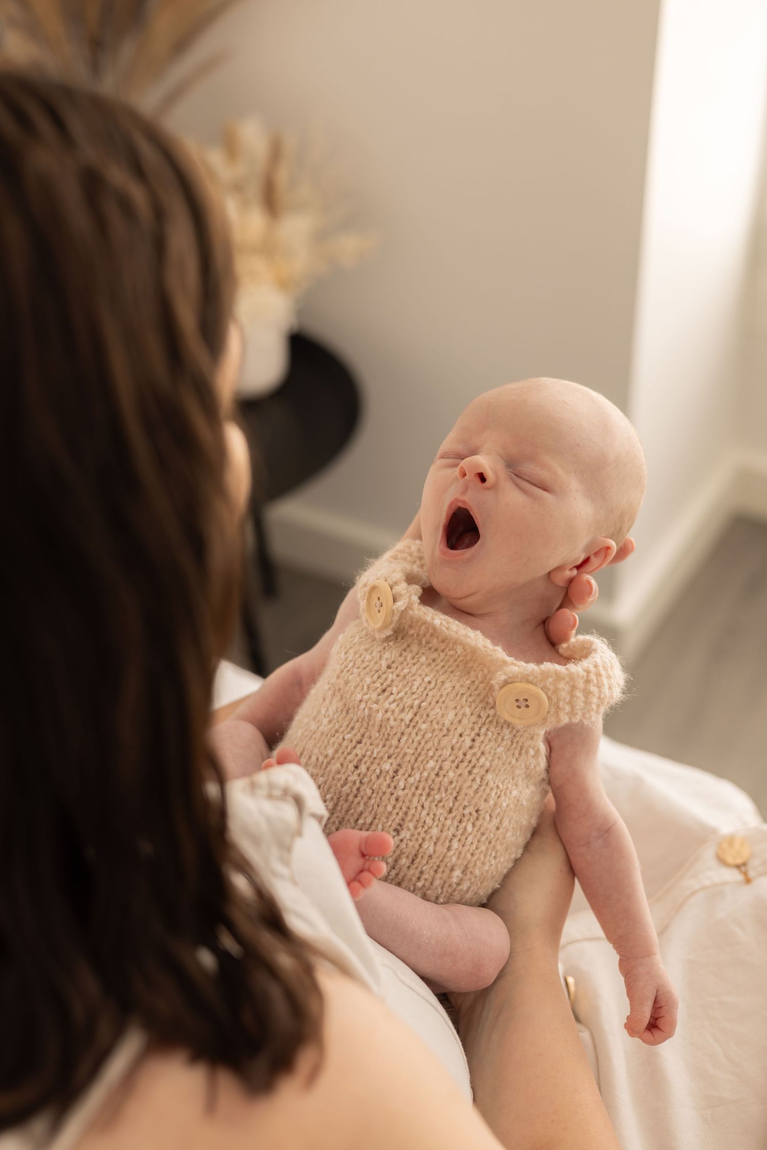 Baby in cream knit romper yawning while being held.