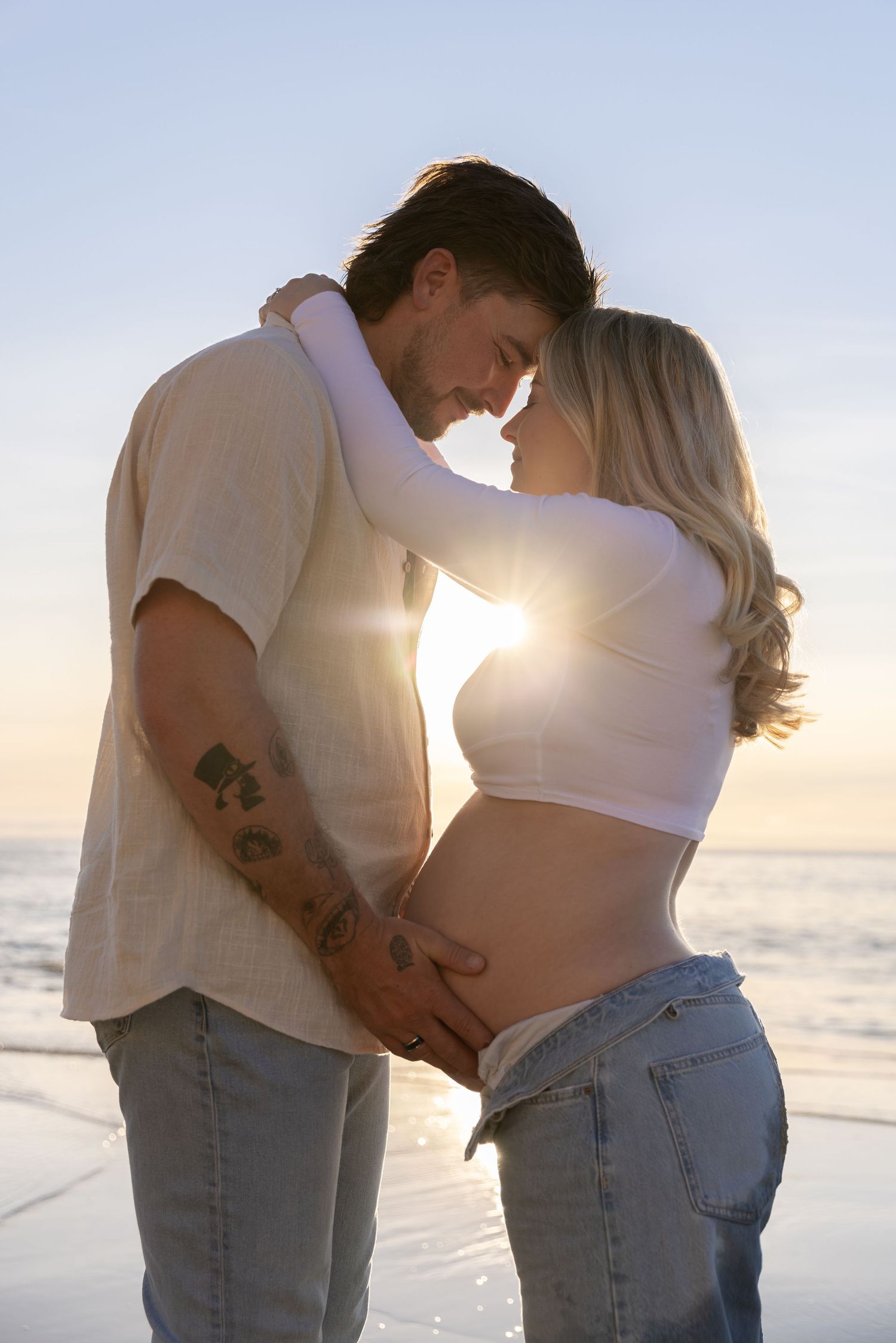 Intimate beach maternity photos of couple embracing with golden sunlight.