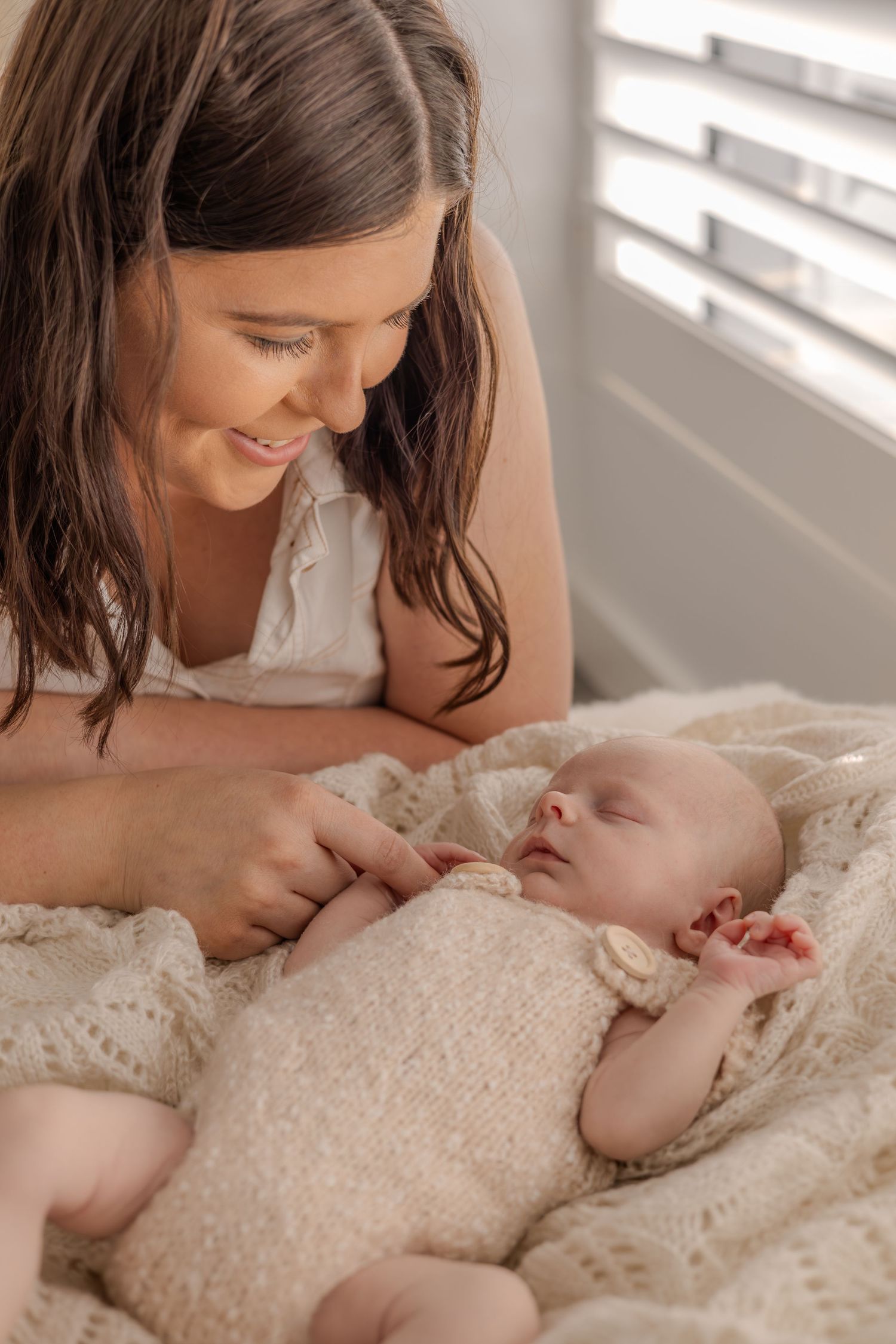 Mother and baby share intimate bonding moment on white bedding near window.