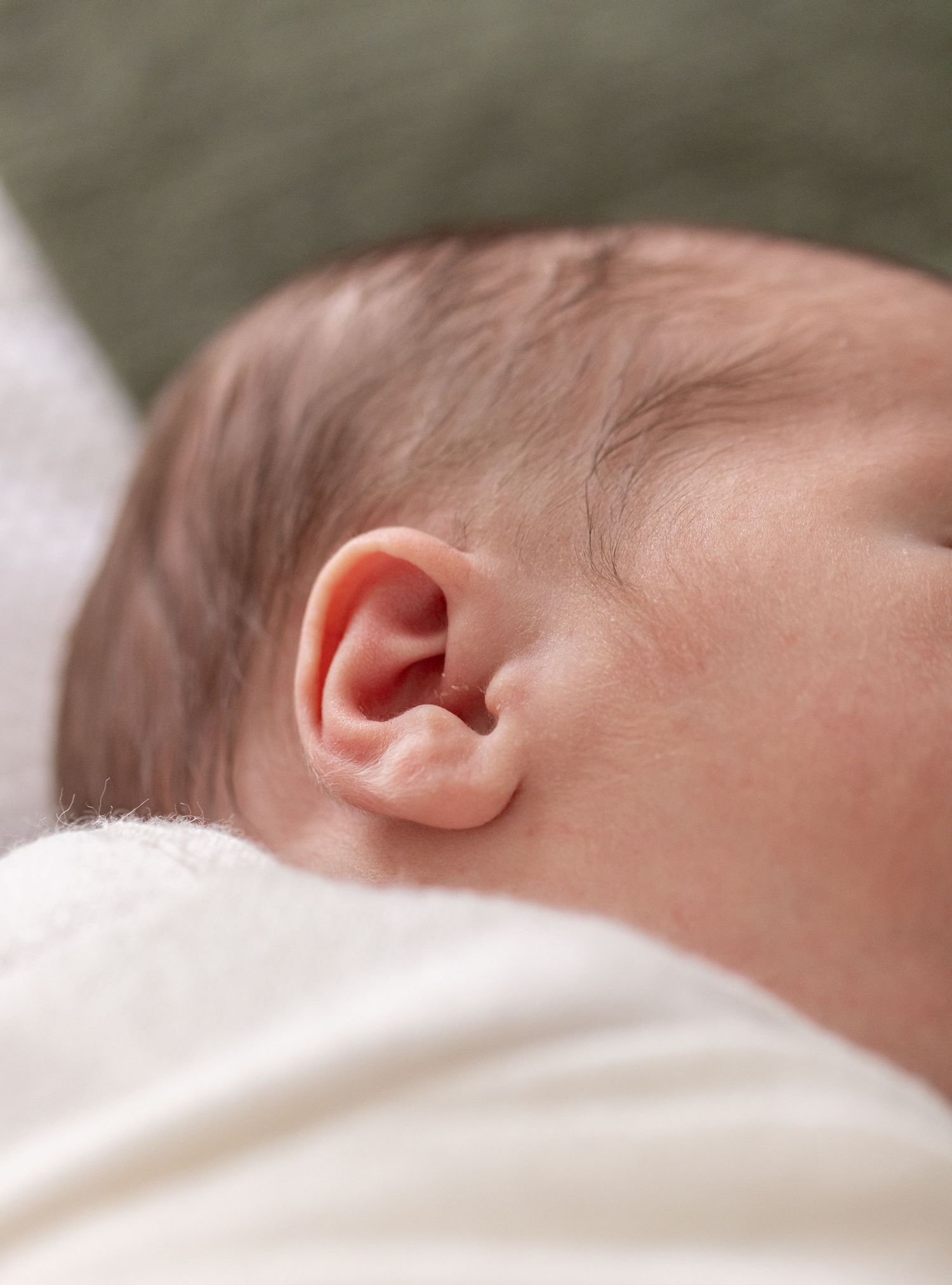 Close-up macro photograph of a newborn baby's ear against white fabric.