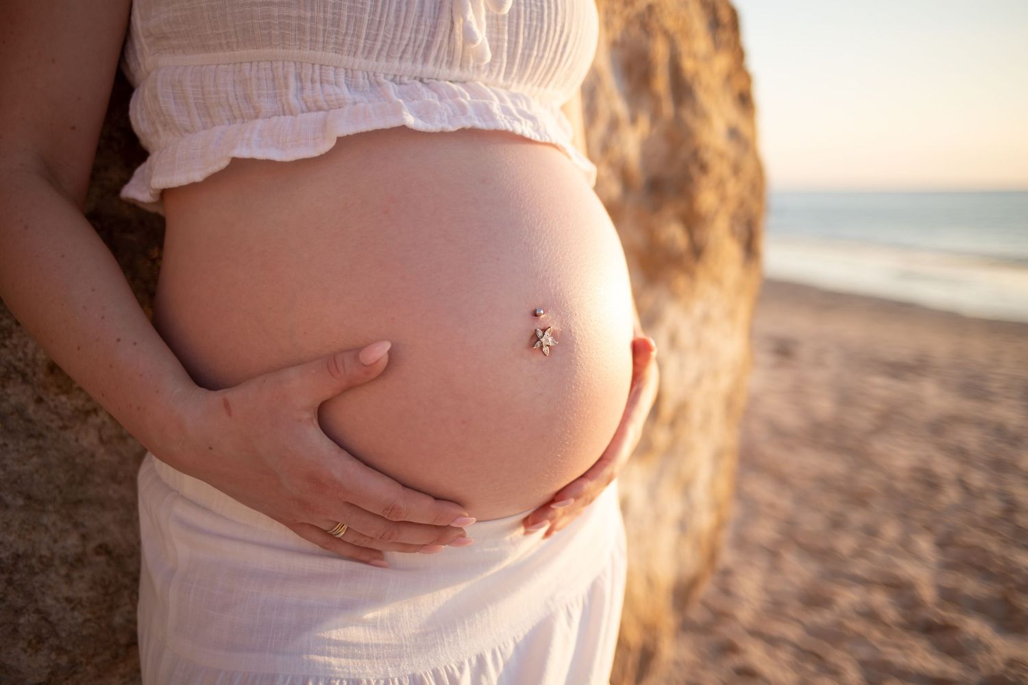 Sunset maternity photo showing belly with belly button ring on beach.