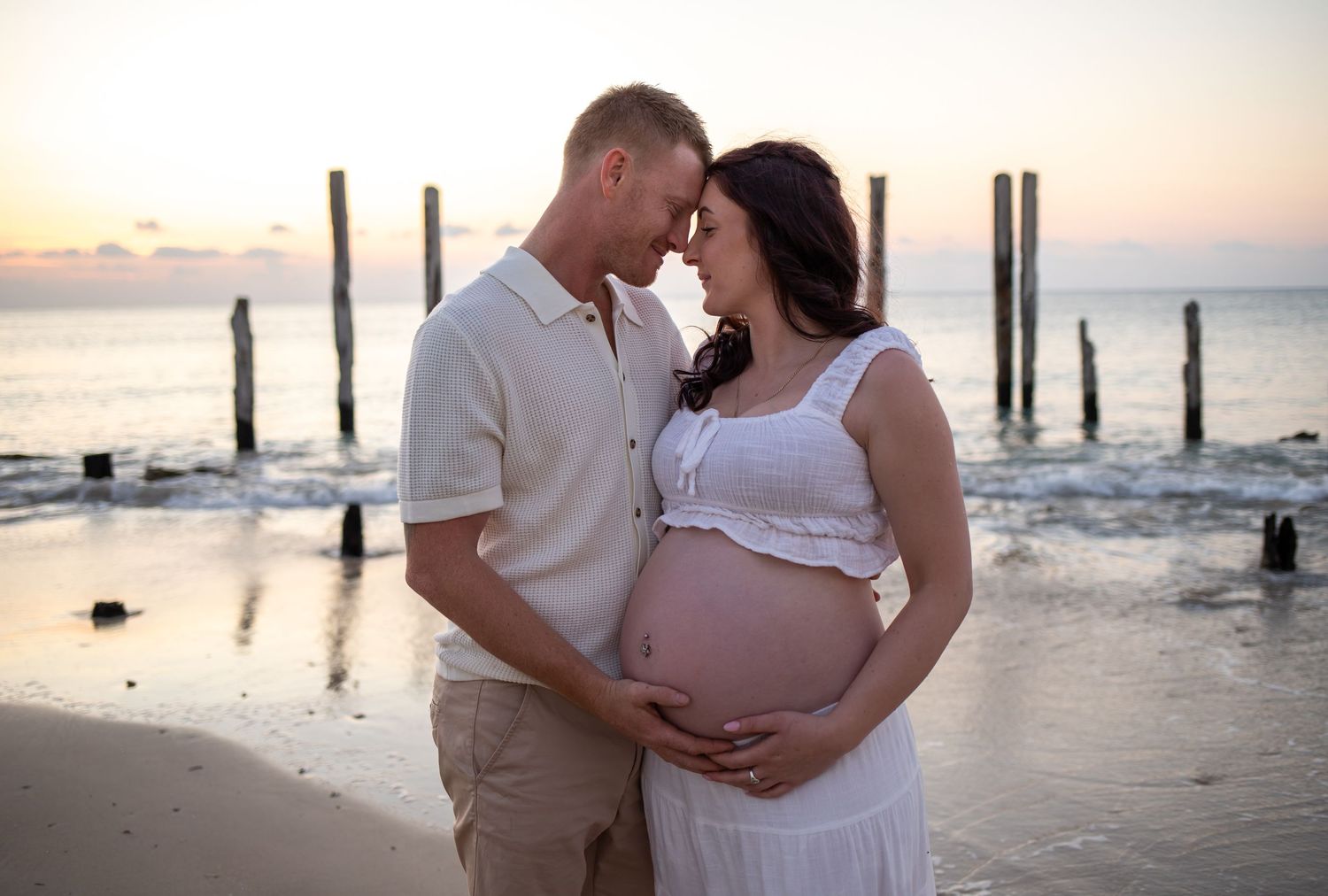 A couple shares an intimate moment on Port Willunga beach at sunset during their maternity photoshoot.