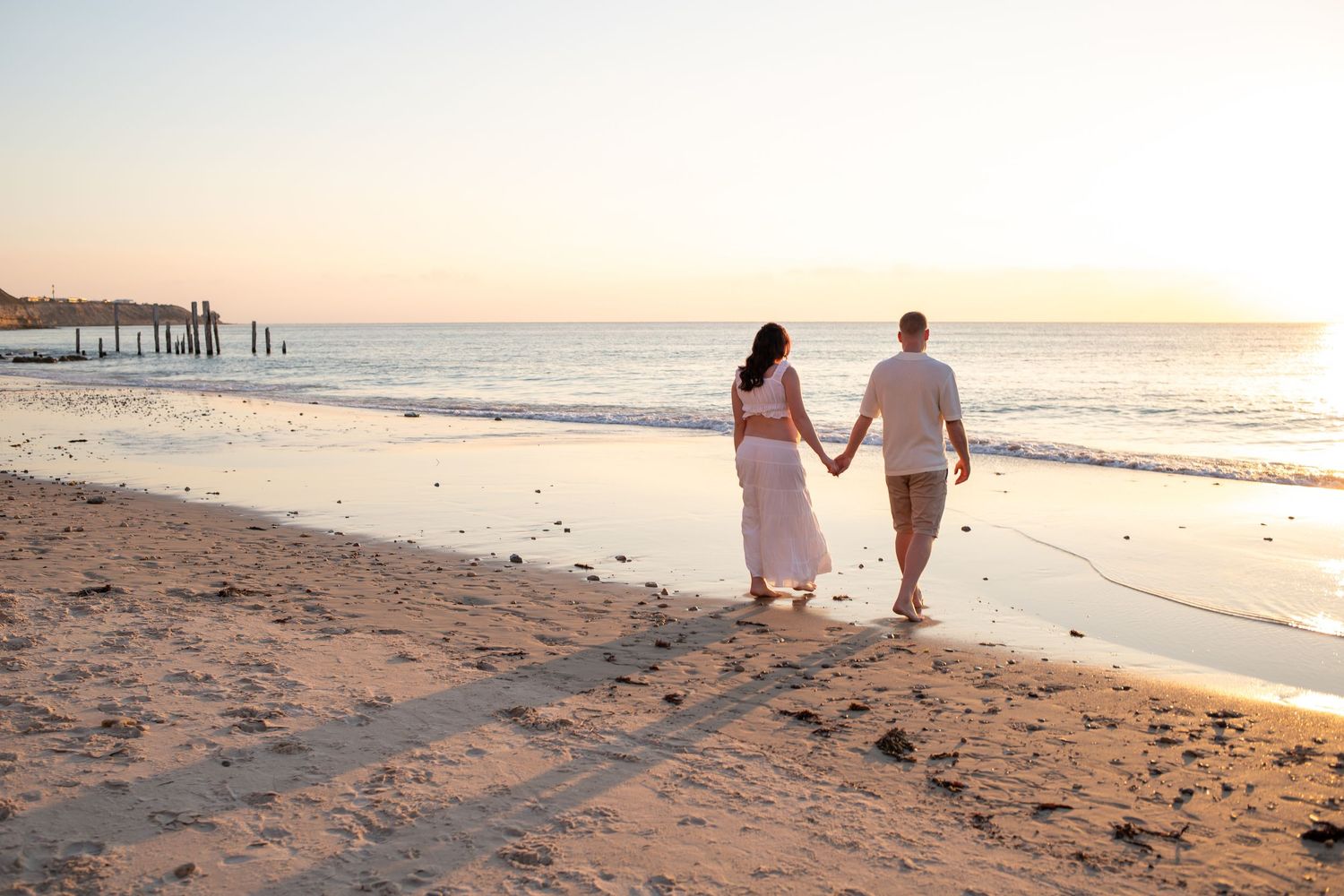 Silhouettes of people walking hand in hand along a peaceful beach at sunset.