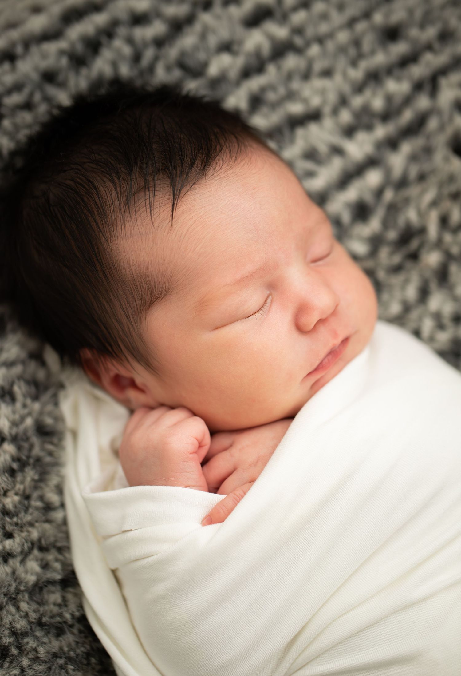 Sleeping baby wrapped in white against grey textured background.