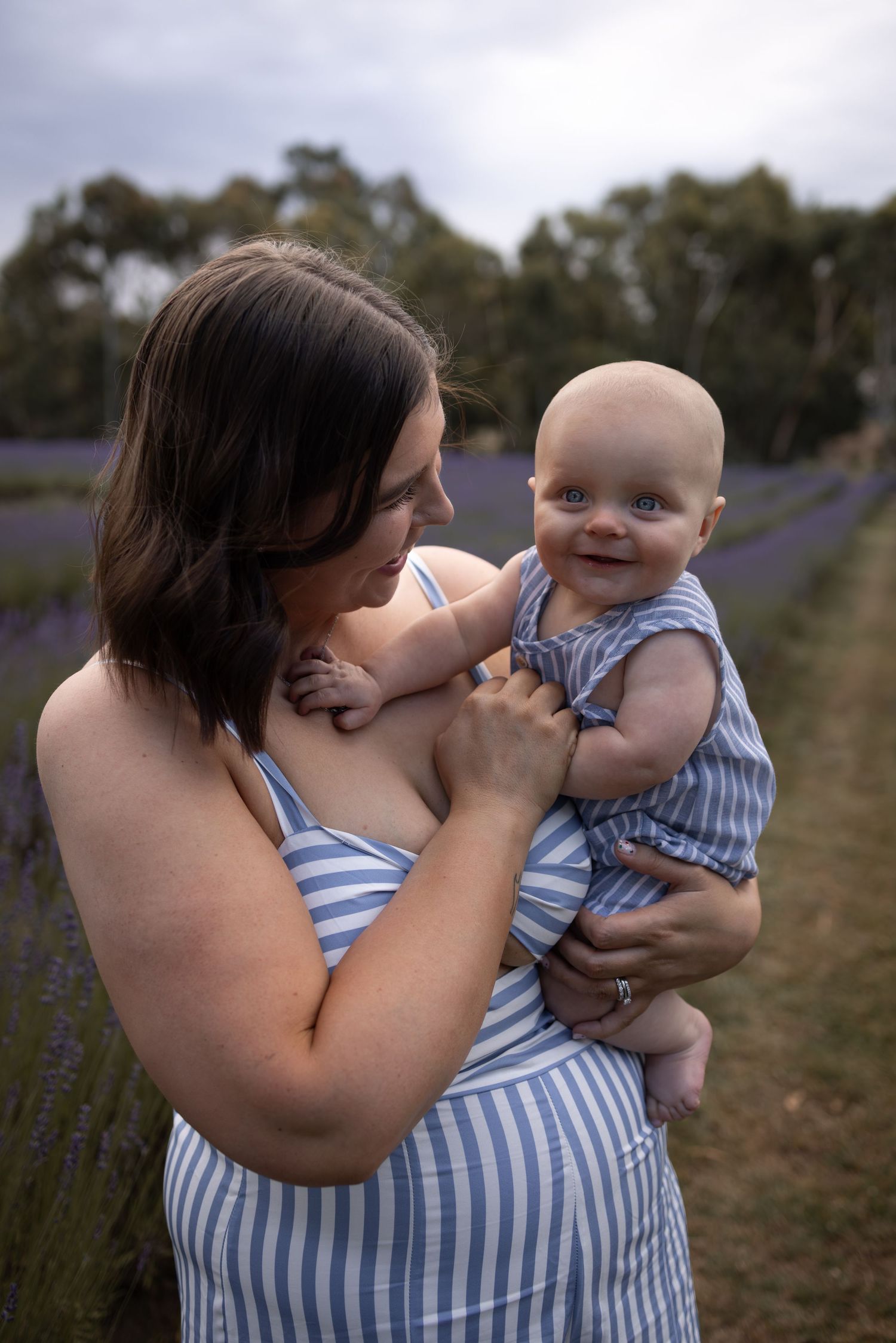 Mother and baby share tender moment in lavender field wearing matching striped outfits.