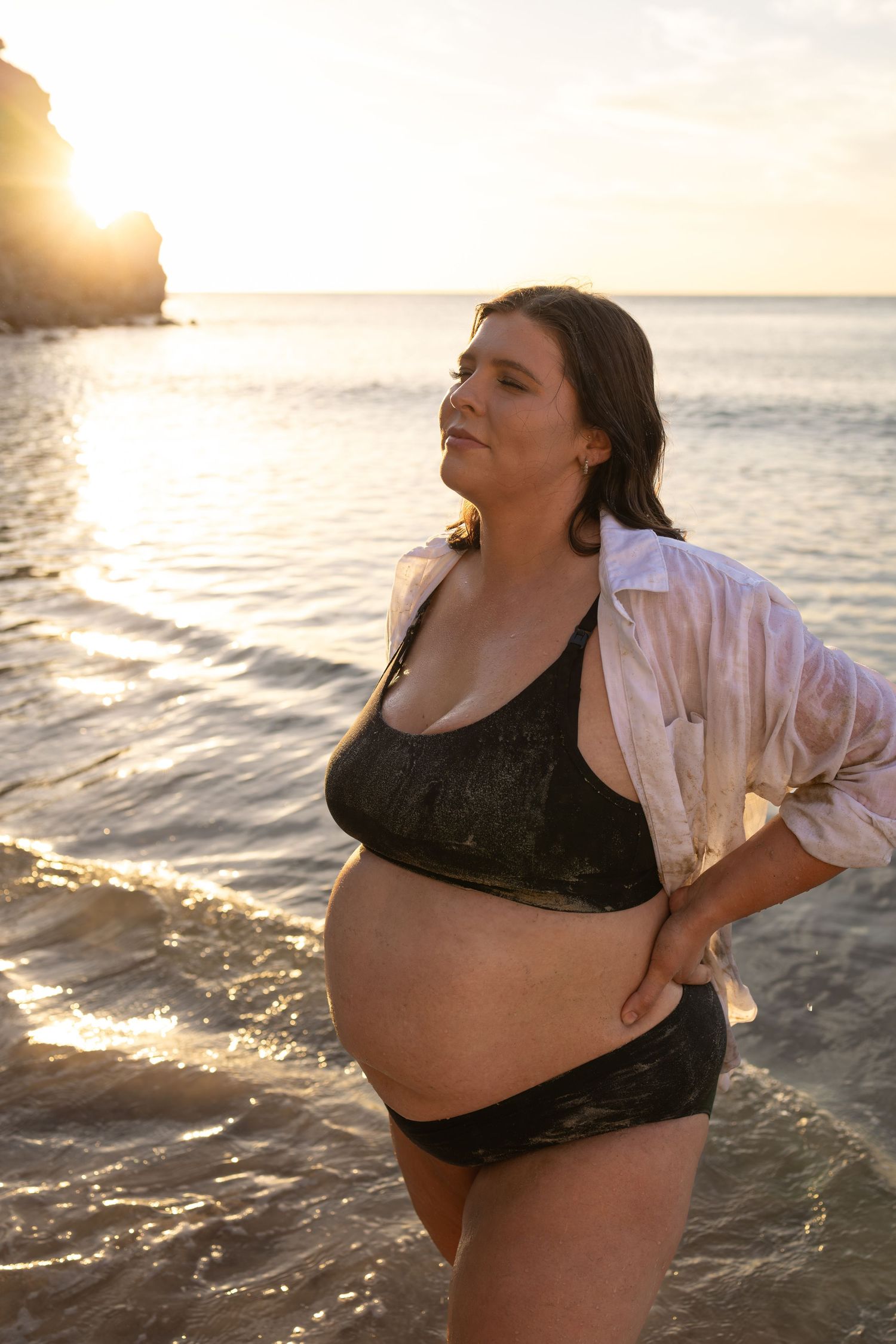 Joyful maternity beach portraits with waves and sunset lighting.
