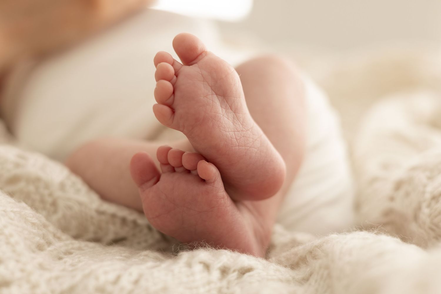 Close up of tiny baby feet resting on soft cream colored textured blanket.
