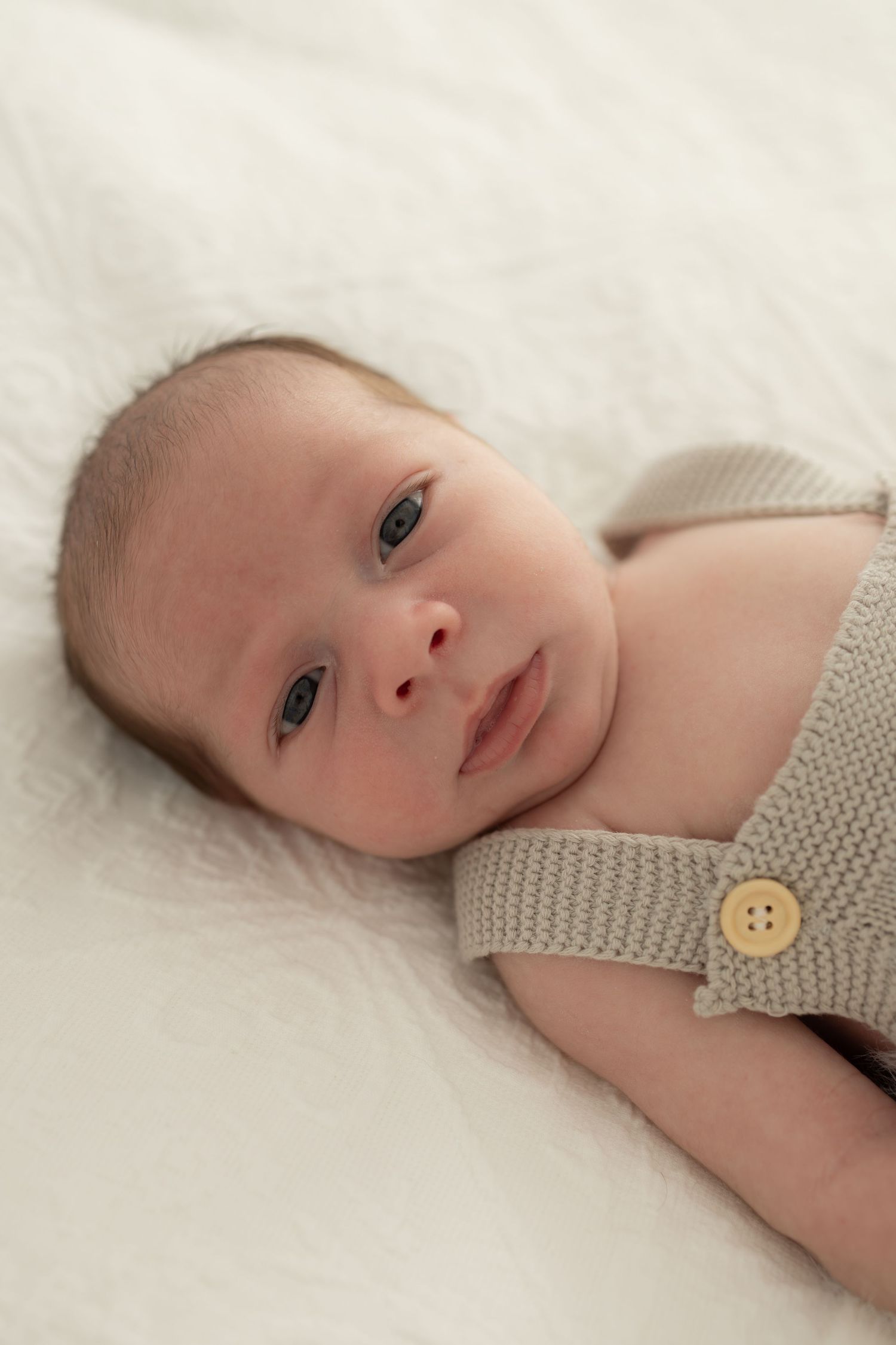 Baby wearing knit romper with button detail lying on white backdrop.