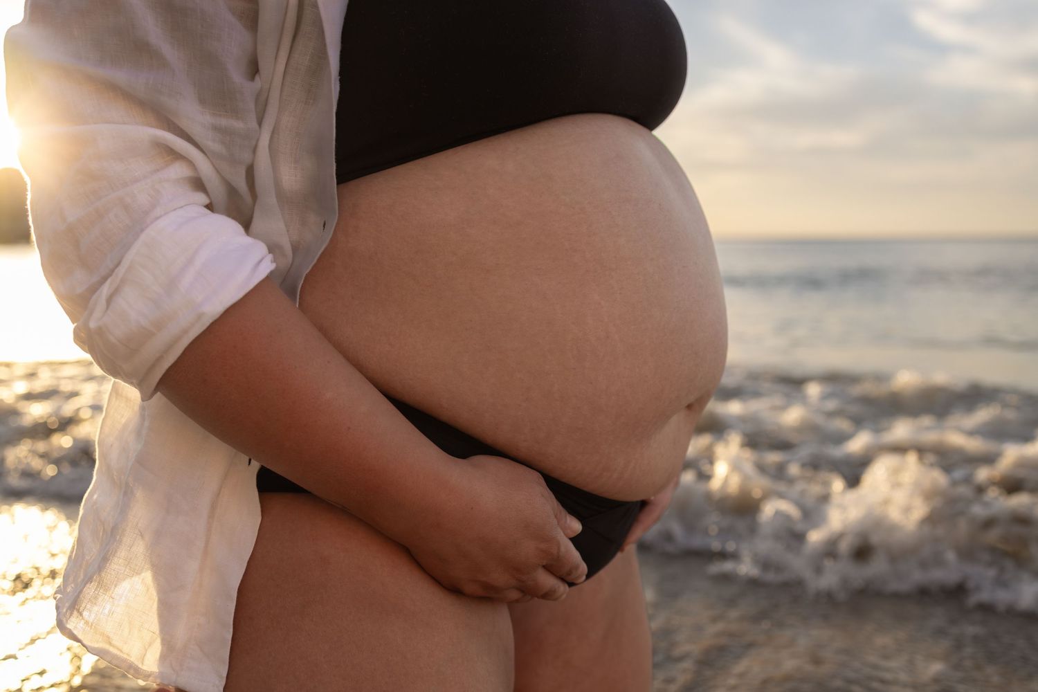 Close-up maternity beach photos showing pregnant belly with waves in background.