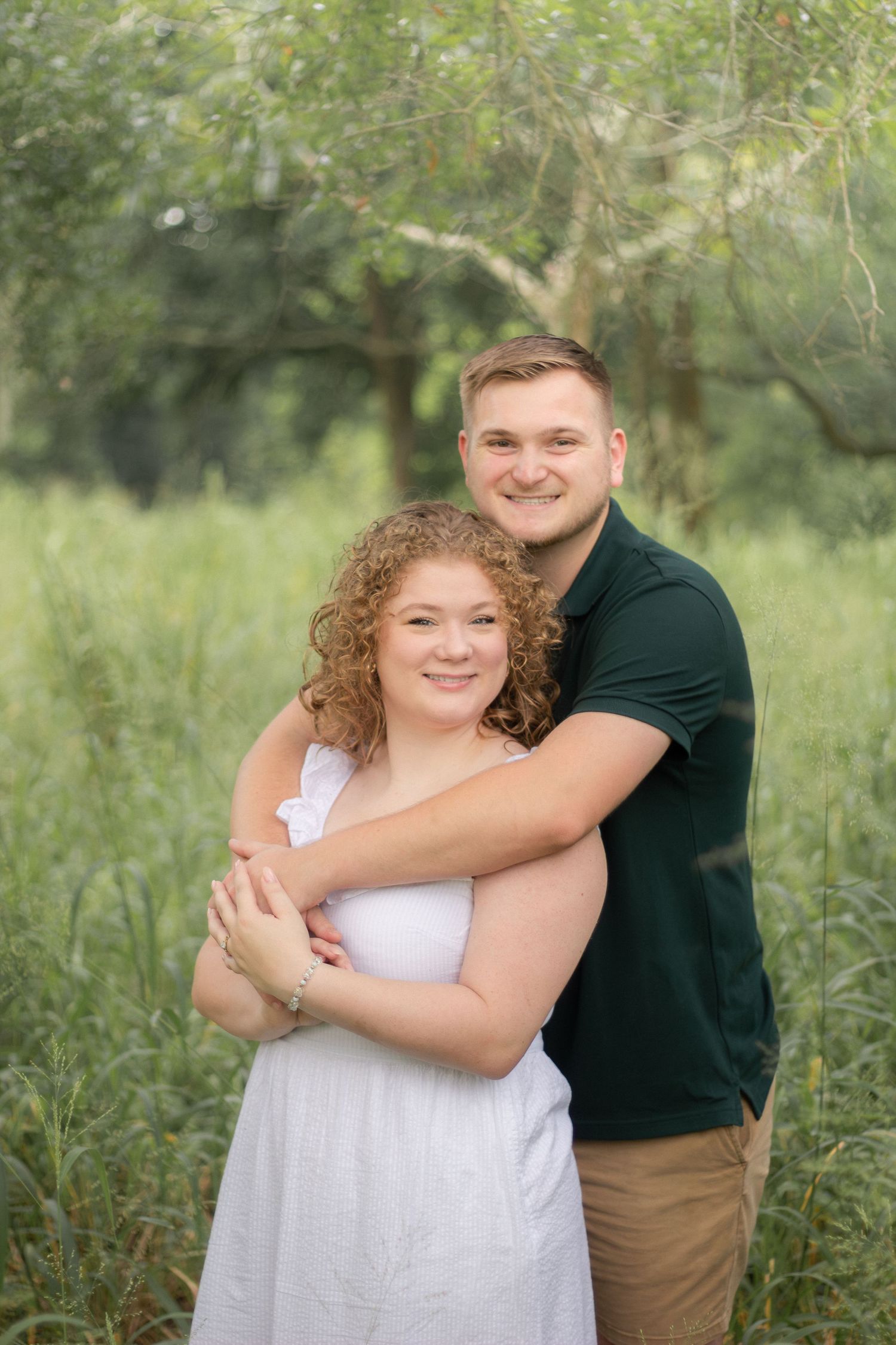 Couple shares warm embraces and smiles during their outdoor photo session in a natural green setting.