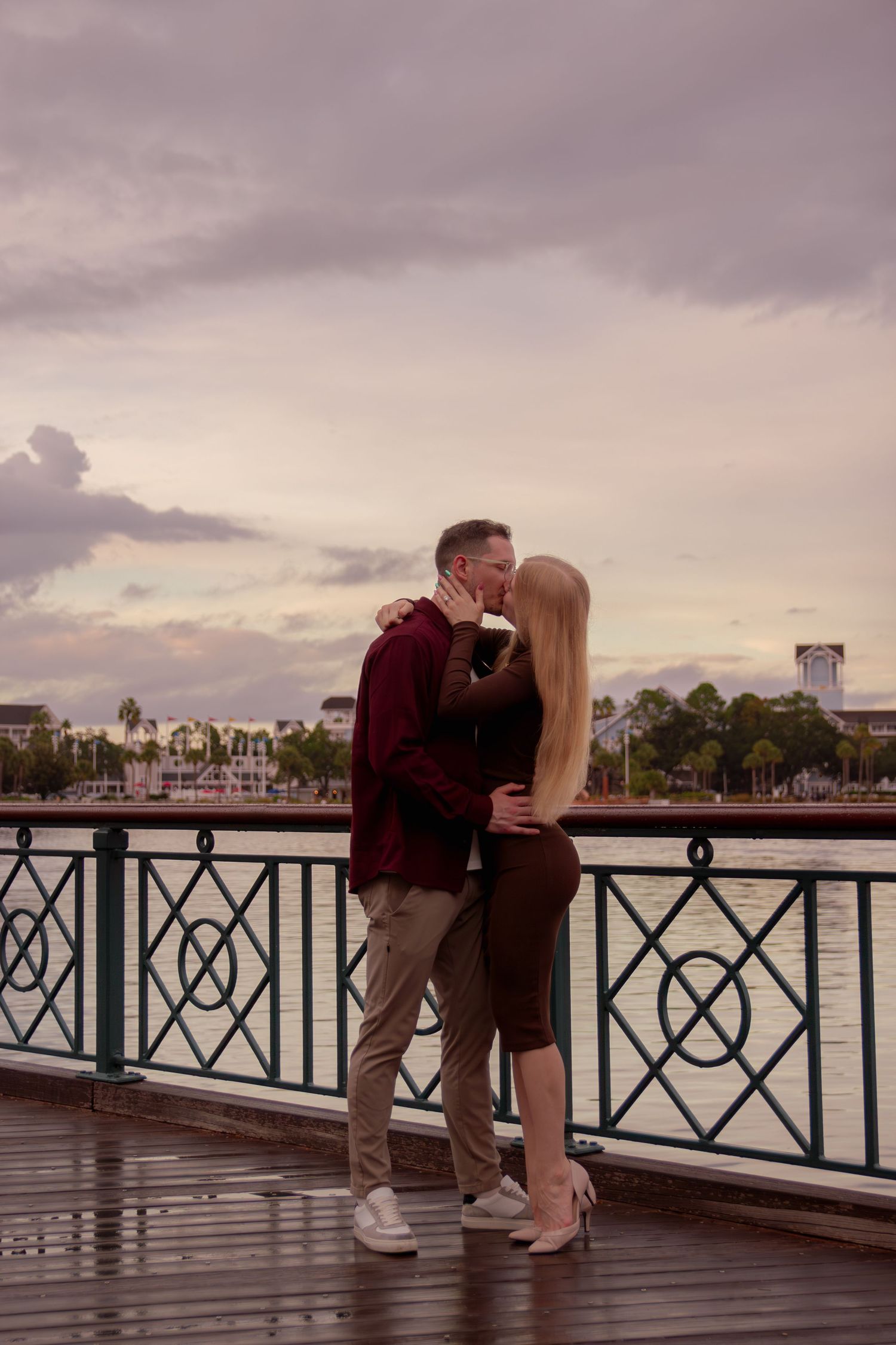 A romantic sunset scene shows a couple embracing on a waterfront boardwalk with boats in the background.