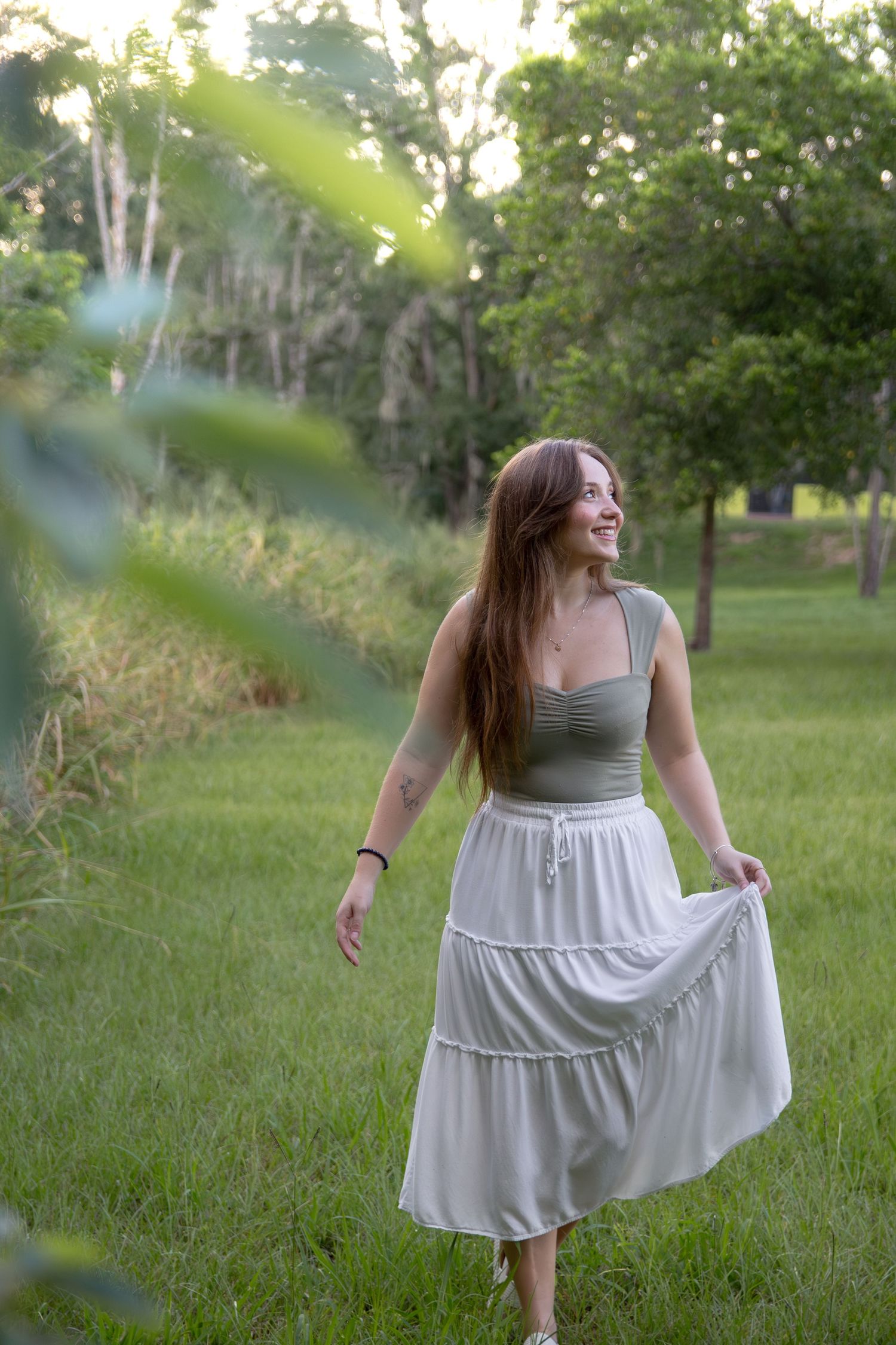 A person in a white sundress twirls joyfully in a green grassy field on a sunny summer day.