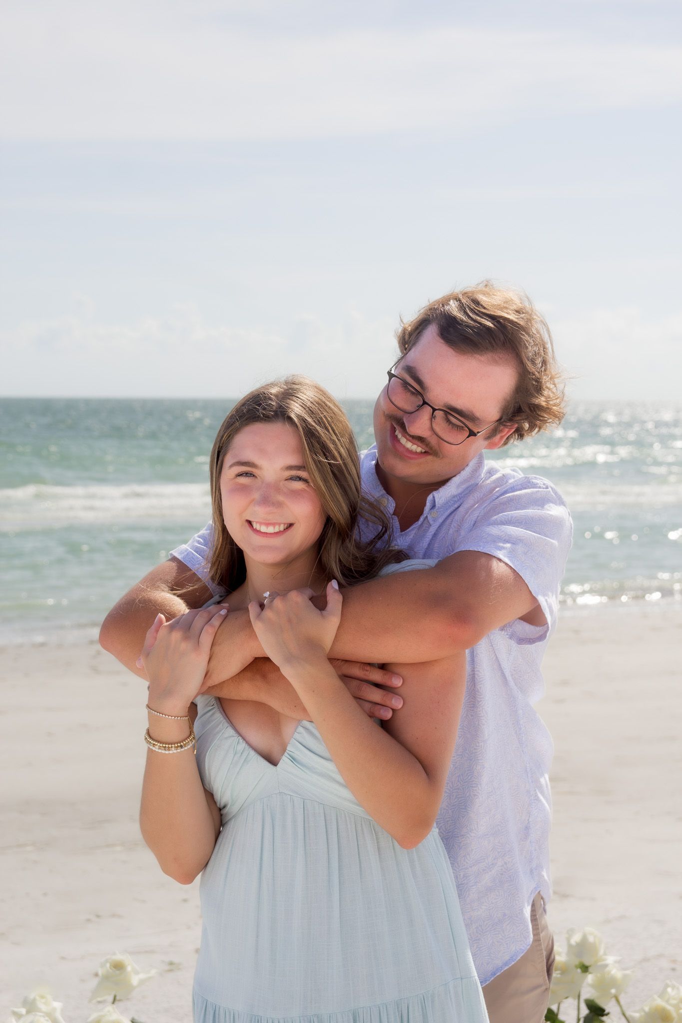 A romantic moment captured between a couple in light blue and white attire on a bright beach.