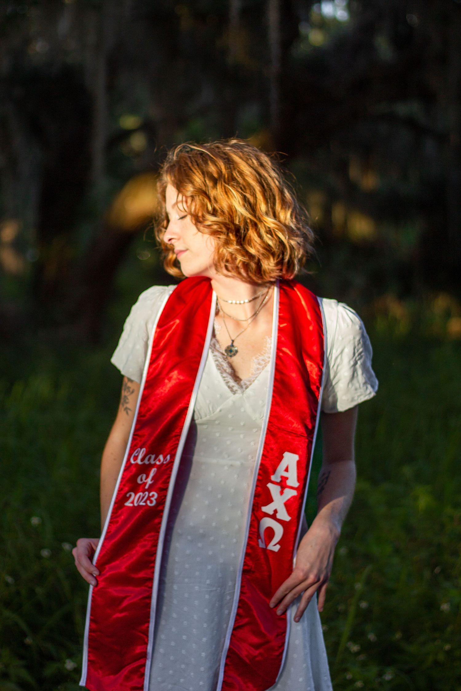 Person wearing a red vest and white shirt stands in a natural outdoor setting with blurred foliage in the background.