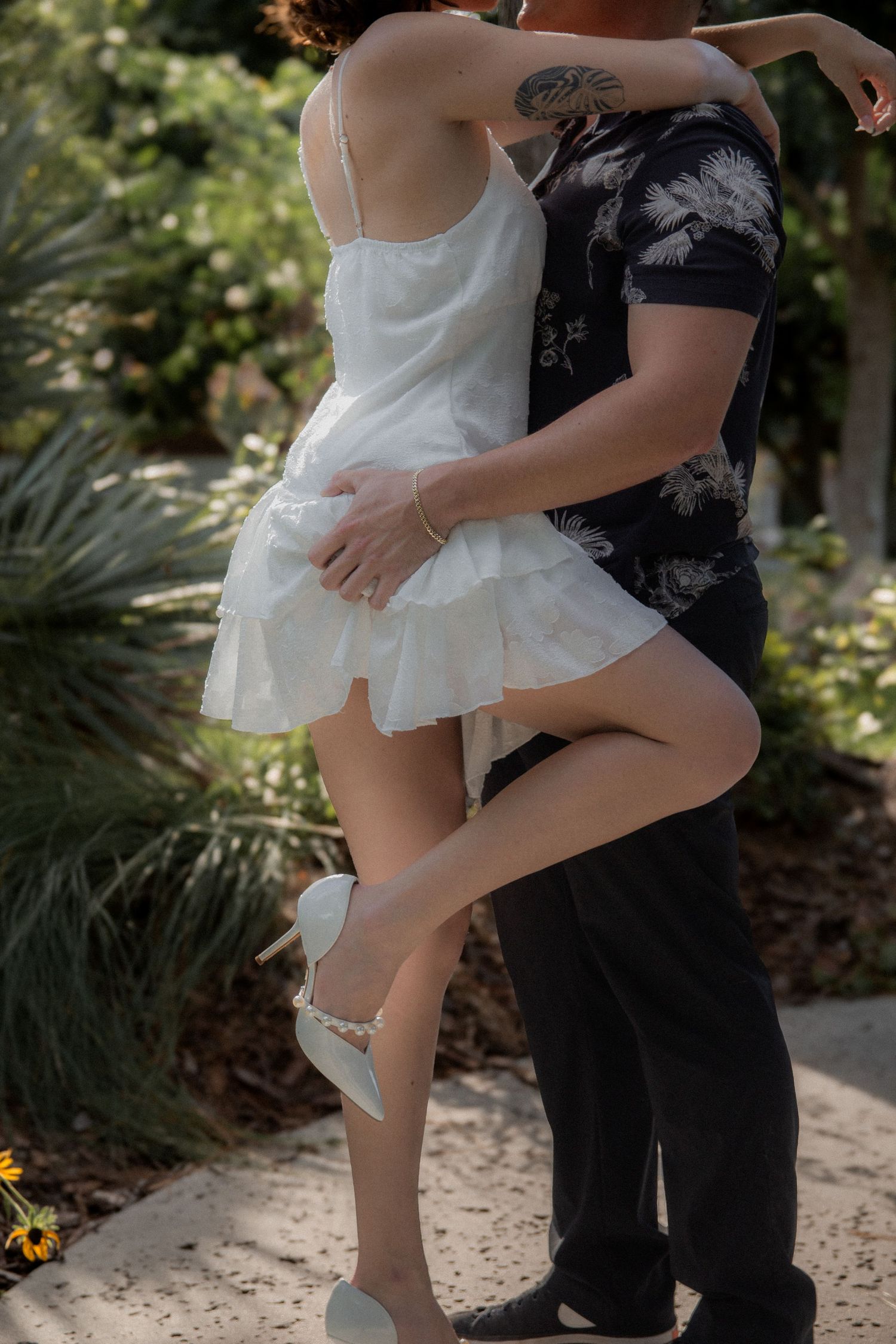 Couple in contrasting white and black outfits dance together in garden setting.
